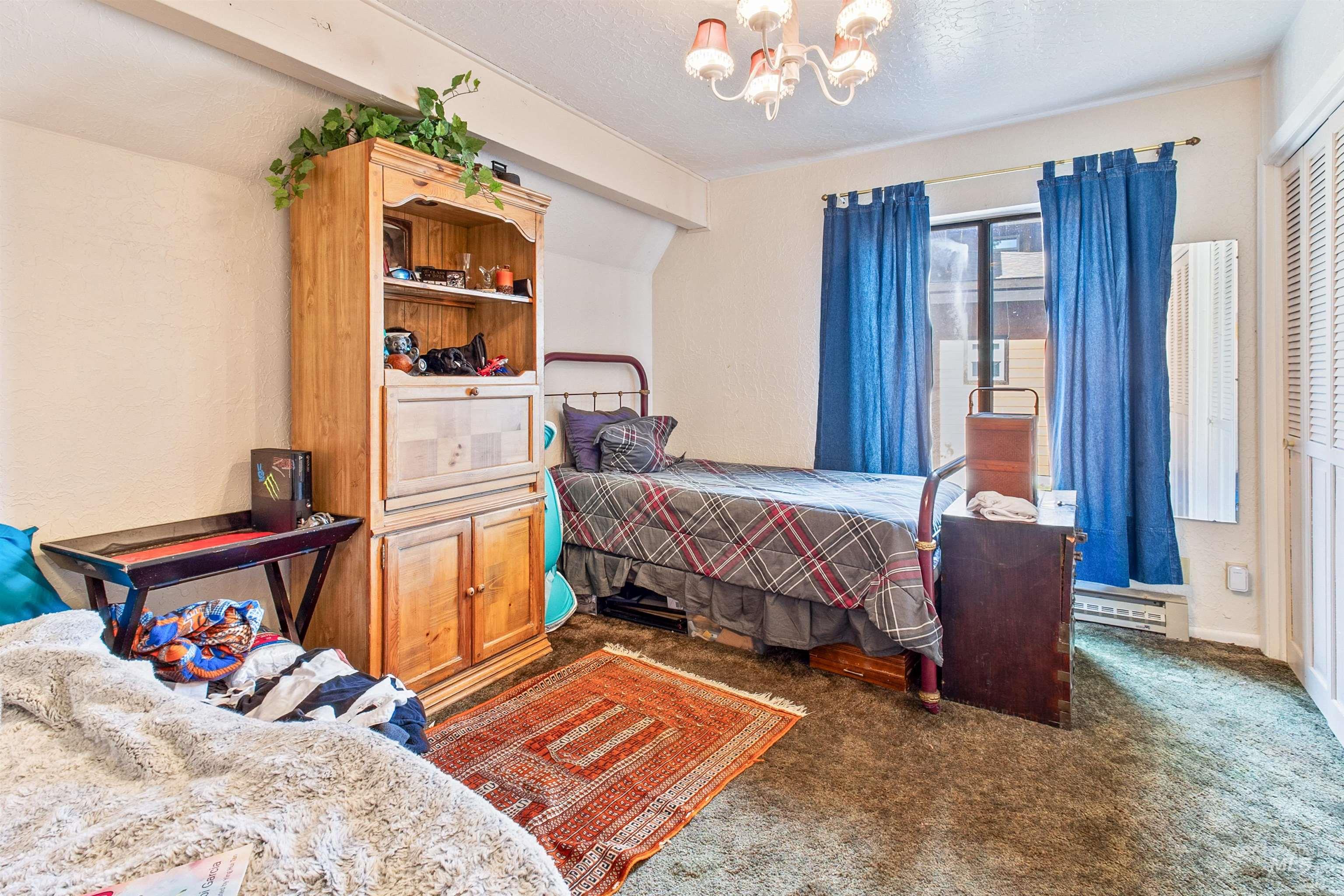 Bedroom featuring dark colored carpet, a chandelier, a baseboard heating unit, and a textured ceiling