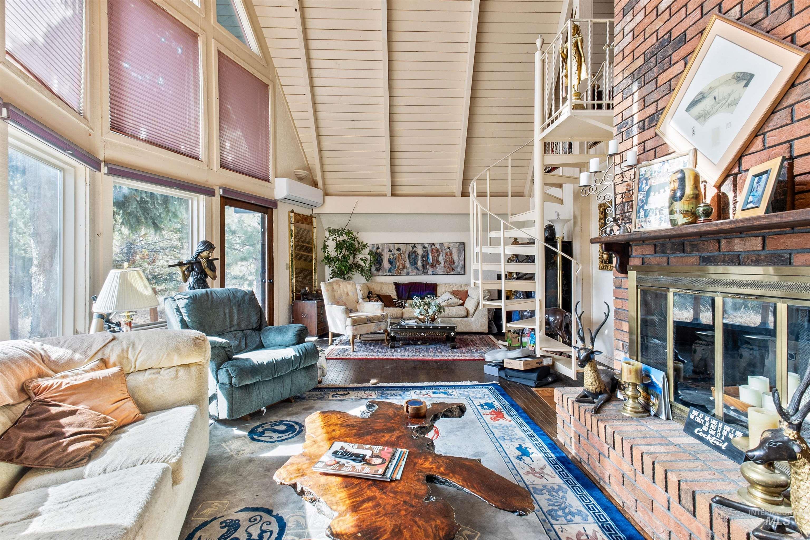 Living area featuring a fireplace, high vaulted ceiling, stairs, a wall mounted AC, and wood finished floors