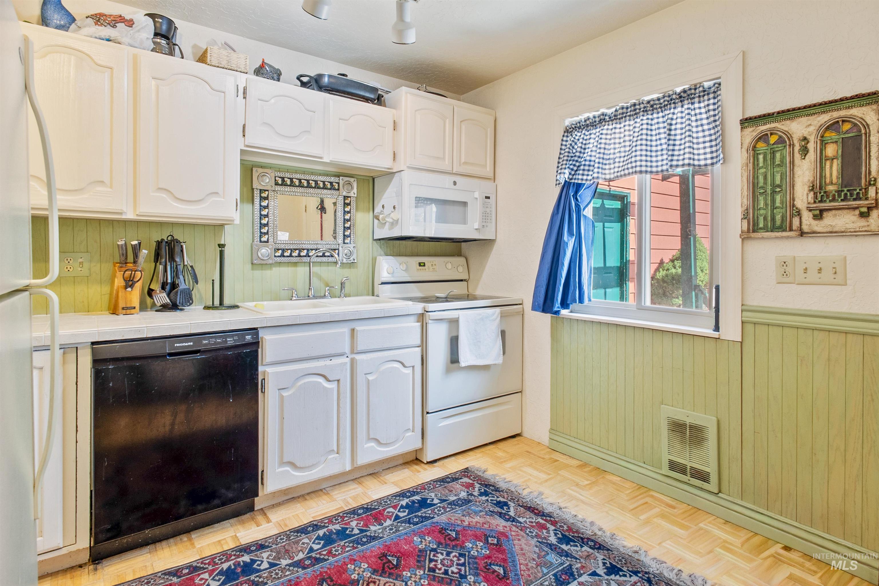 Kitchen featuring tile countertops, white appliances, wooden walls, white cabinets, and wainscoting