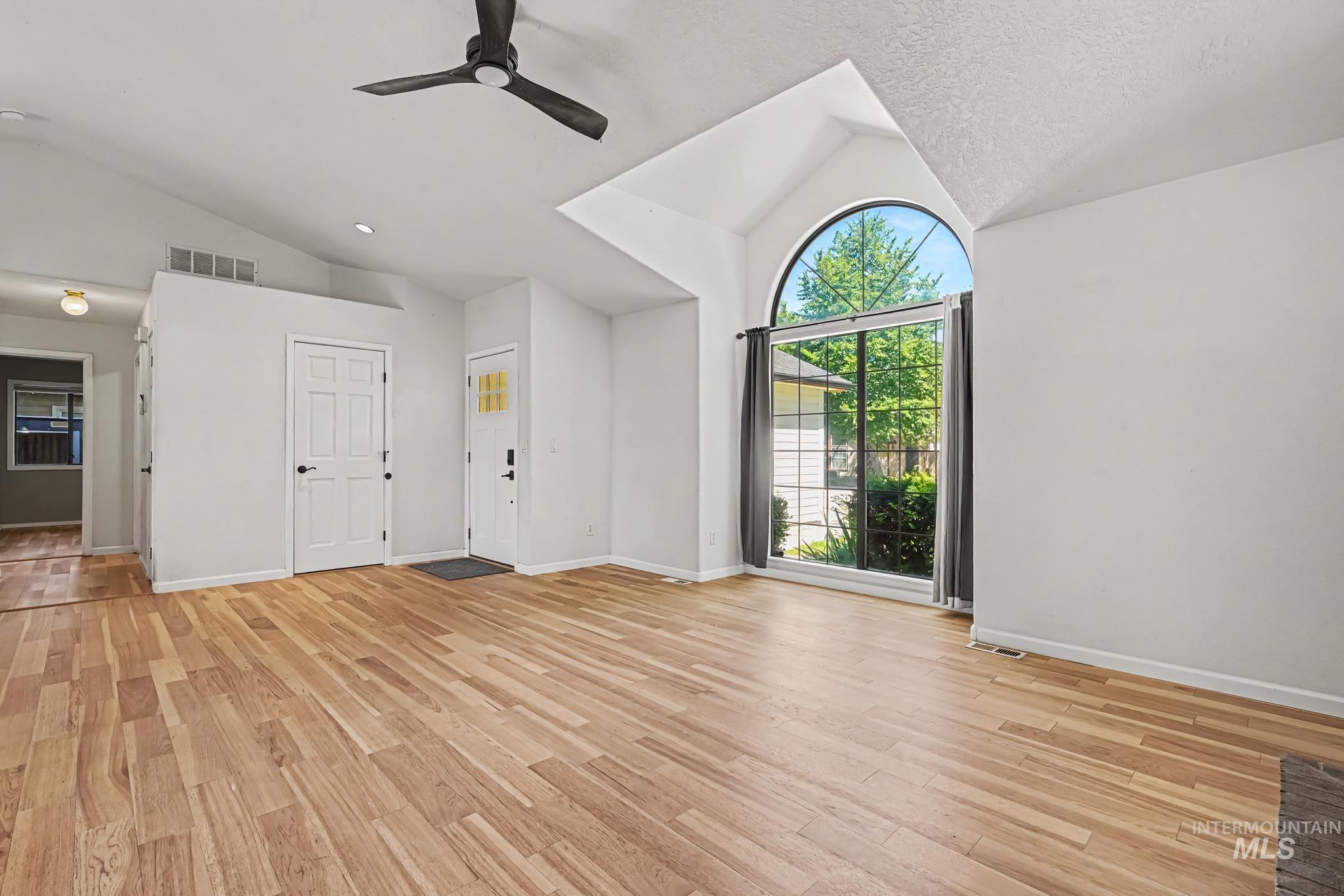 Spacious living area featuring wood-finish flooring, vaulted ceilings, and a large arched picture window