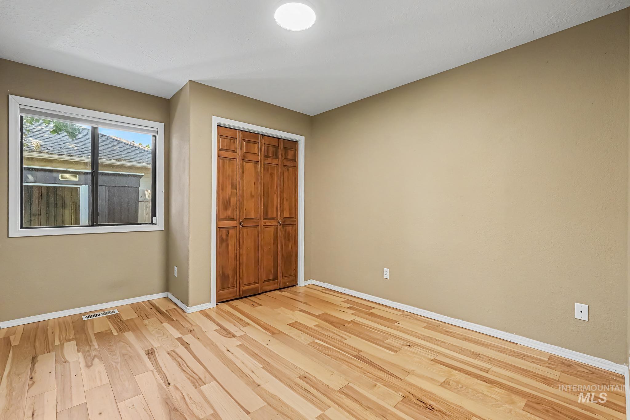 Room with light wood-finish flooring, a window with white trim, a built-in closet with bi-fold wood doors, and neutral-toned walls
