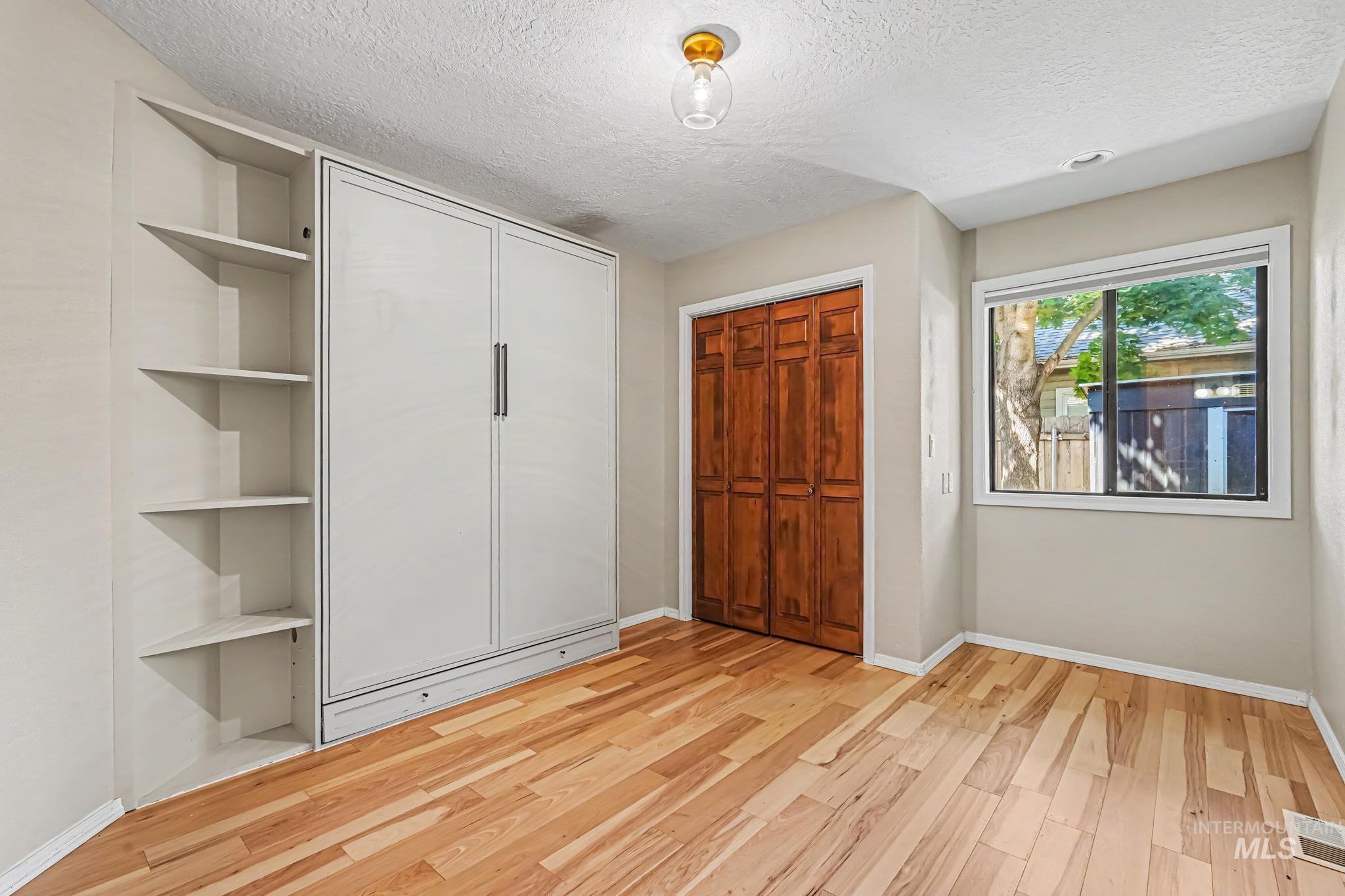Room featuring built-in cabinetry with shelving, wood-finish flooring, and a large window. Custom built in Murphy bed.