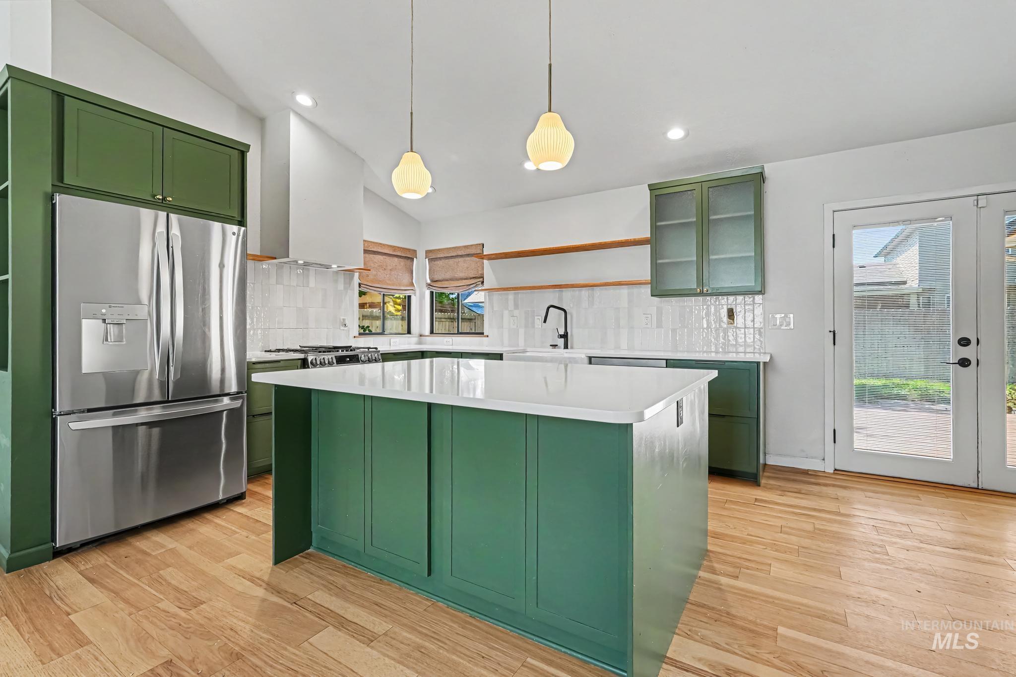 Bright kitchen featuring bold green cabinetry, stainless steel refrigerator, white subway tile backsplash, and light wood-finish flooring