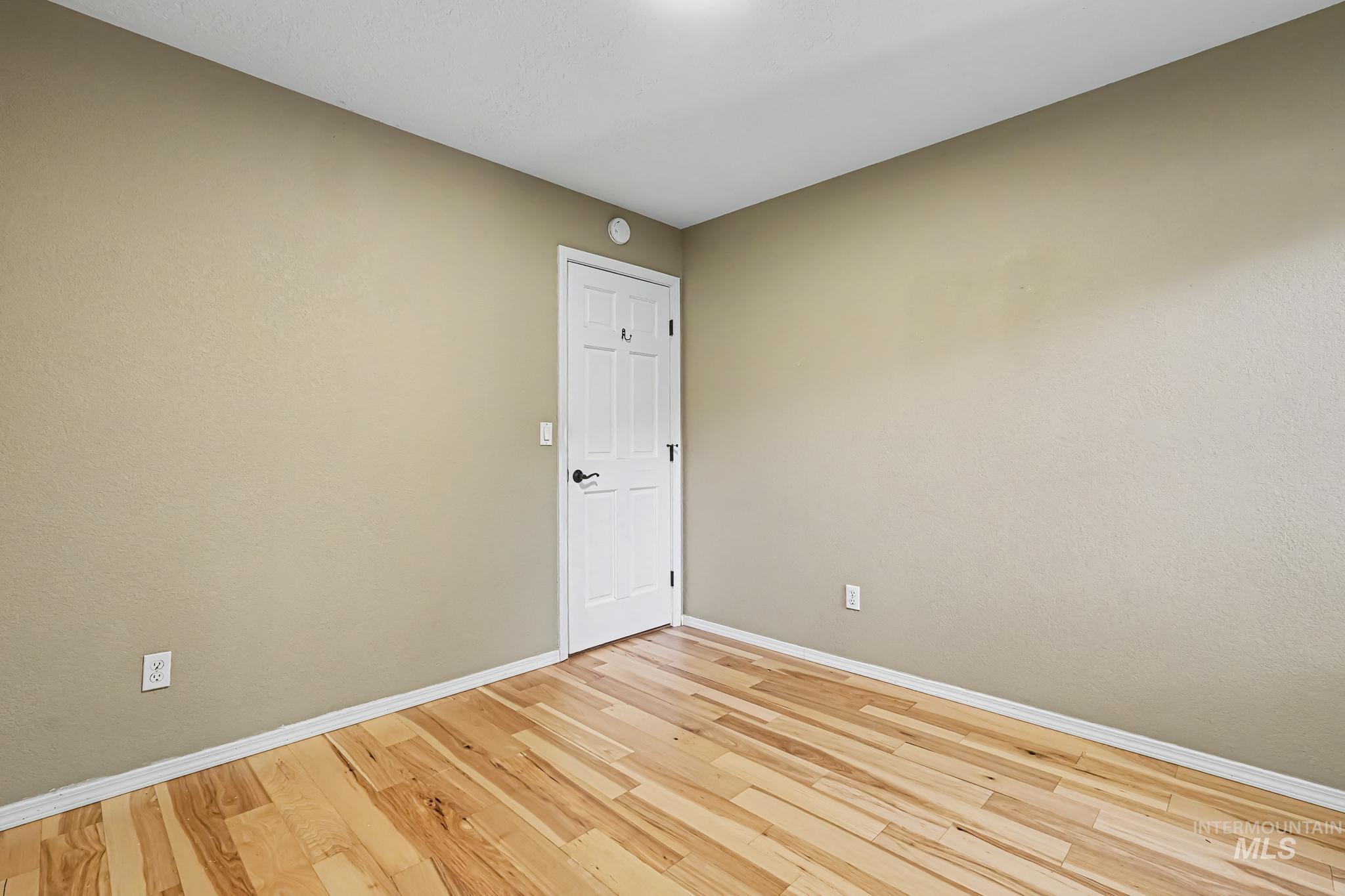 Interior room featuring wood-finish flooring, light tan walls, and a white interior door