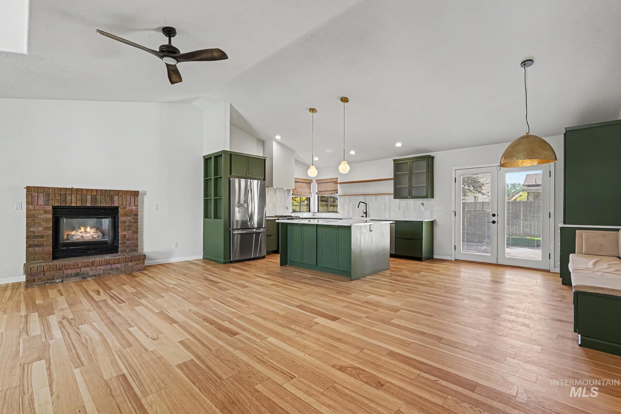 Open-concept living space featuring wood-finish flooring, a brick fireplace, and vaulted ceilings