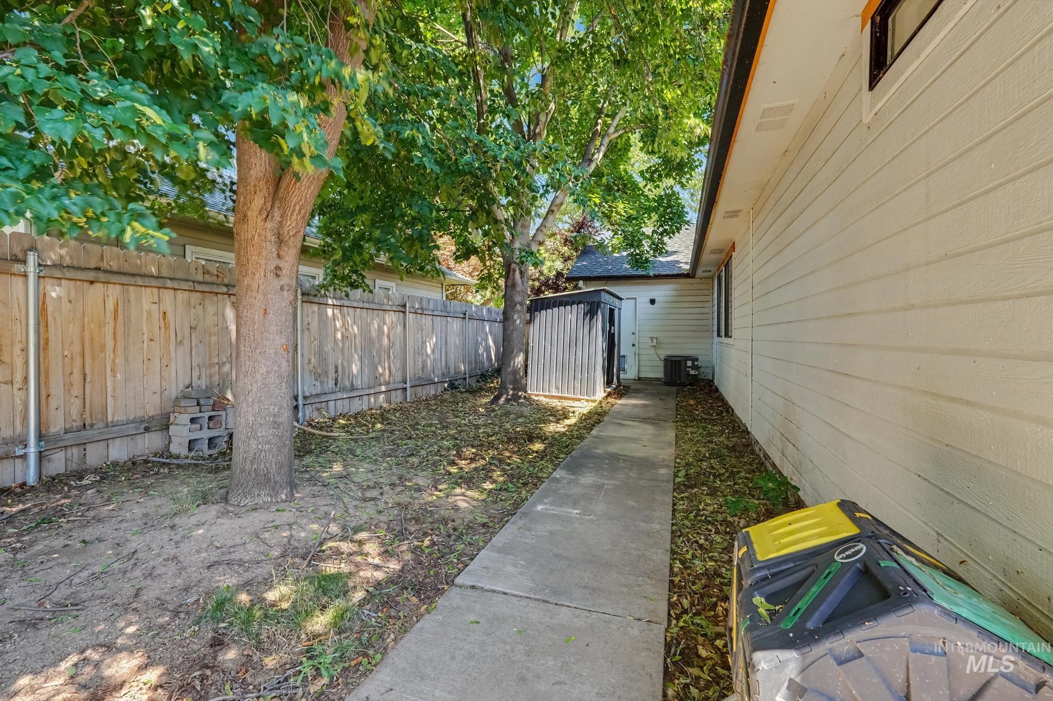 Side yard featuring a concrete pathway, mature trees, and a privacy fence