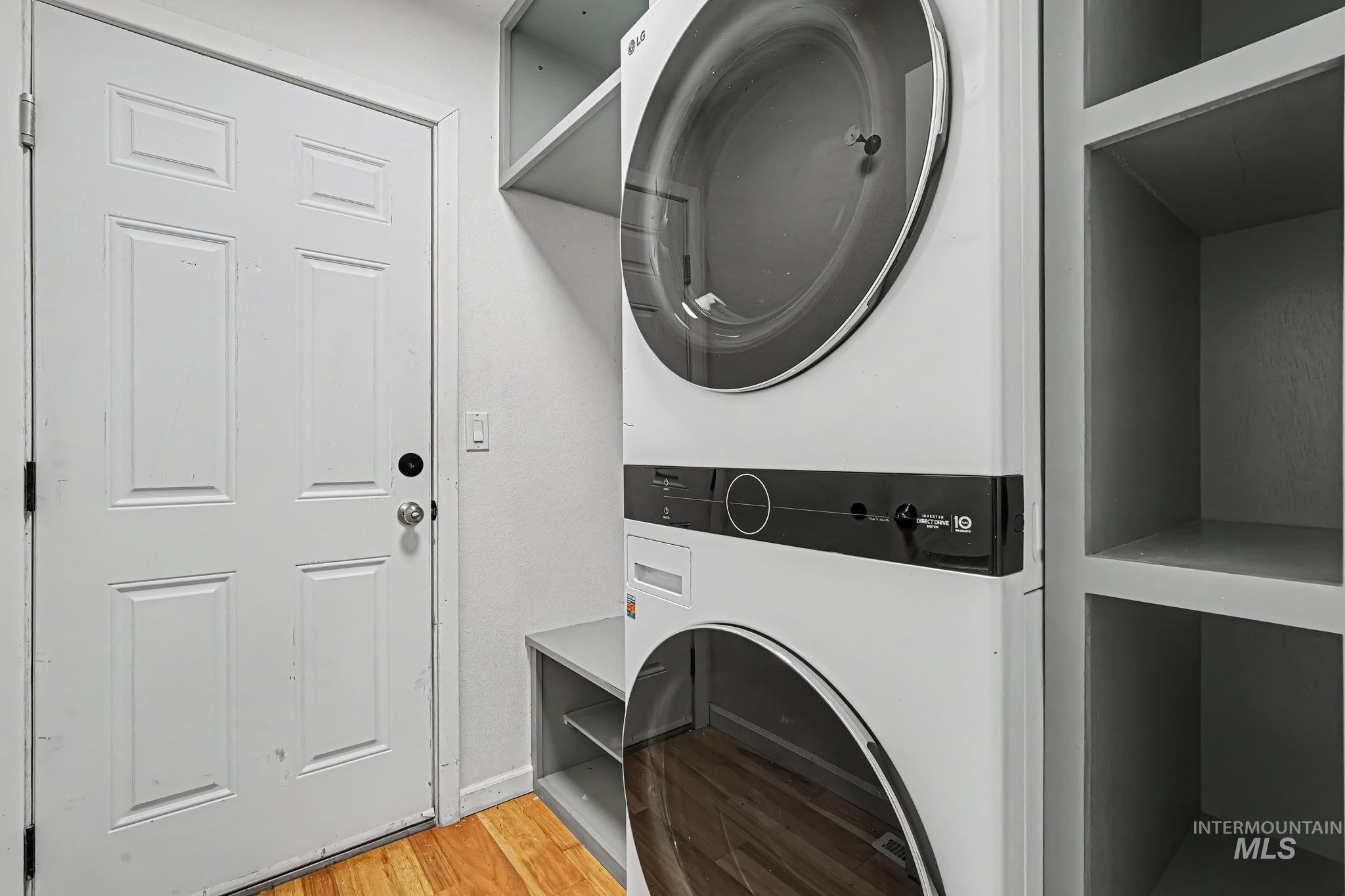 Laundry area featuring a stacked washer and dryer unit, built-in shelving, and wood-finish flooring