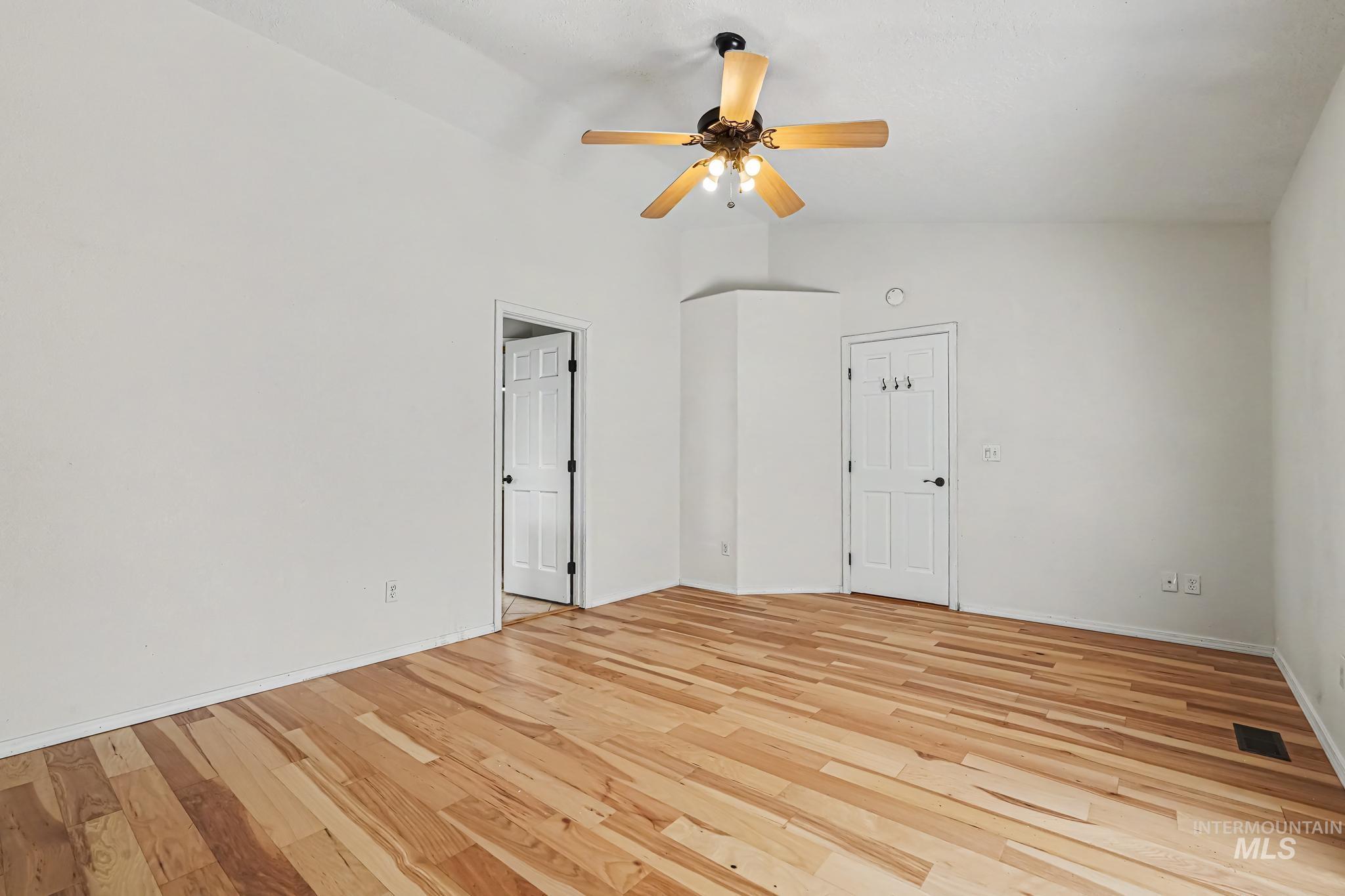 Spacious room featuring wood-finish flooring, vaulted ceiling, and a ceiling fan with integrated lighting