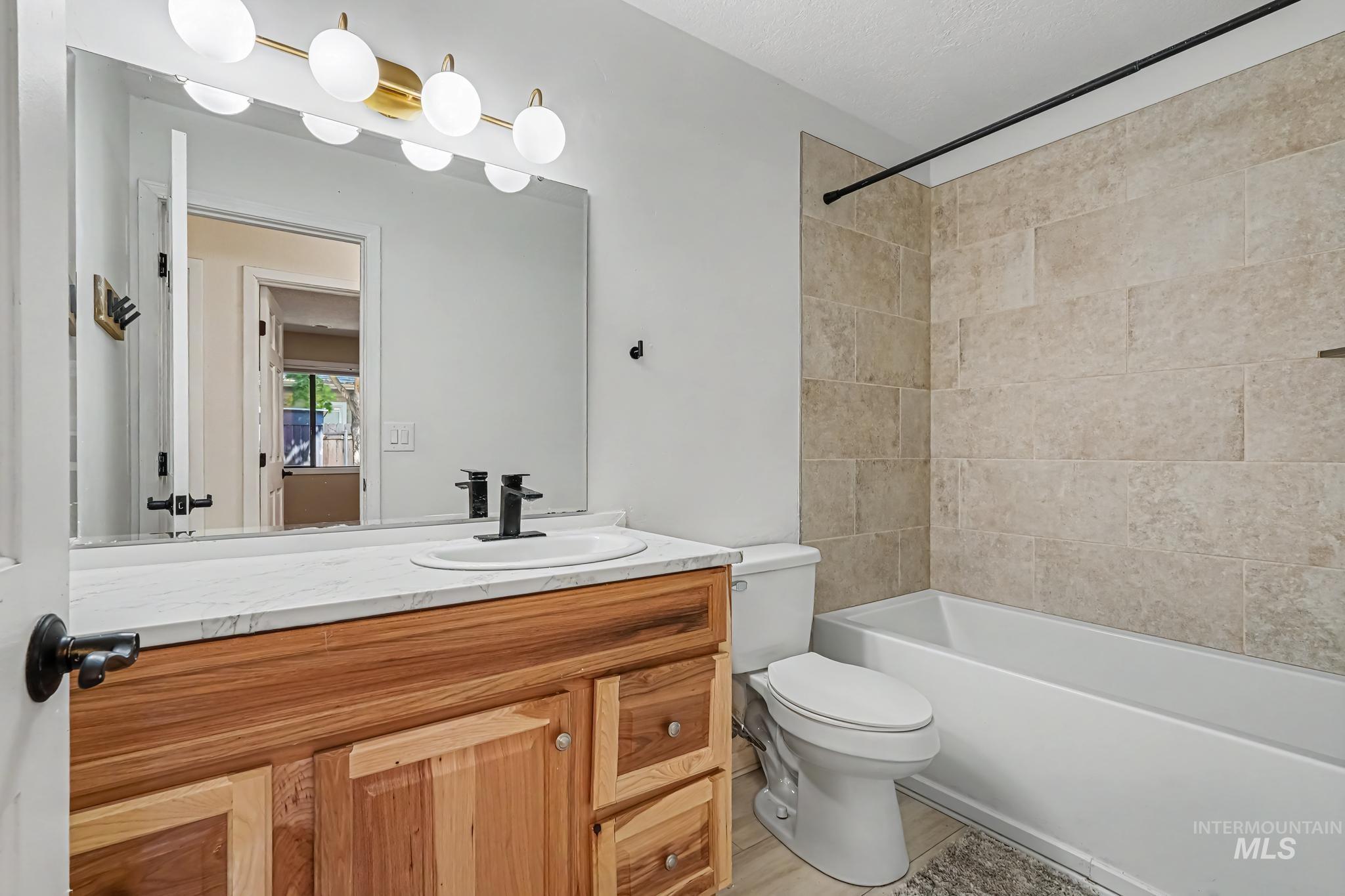 Bathroom featuring a natural wood-finish vanity with a white countertop, a drop-in sink with a matte black faucet, and a large mirror