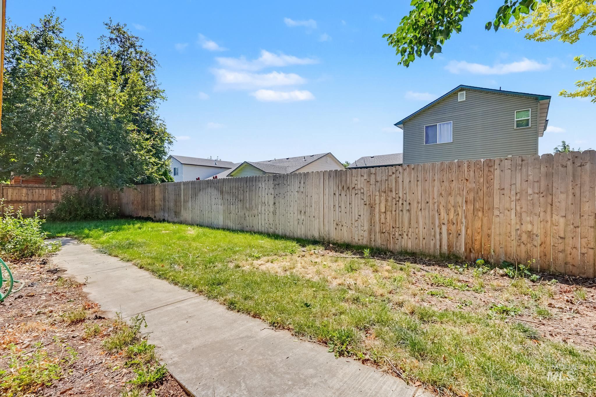 Expansive backyard with a full perimeter wood privacy fence, featuring a concrete pathway and established green foliage