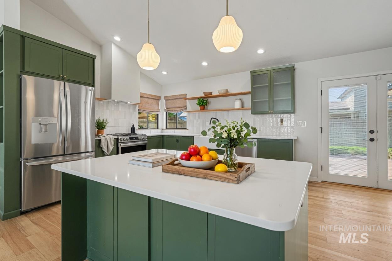 Kitchen featuring a central island with quartz countertop, green cabinetry, stainless steel appliances, wood-finish flooring, and French doors. *Virtually Staged photo*