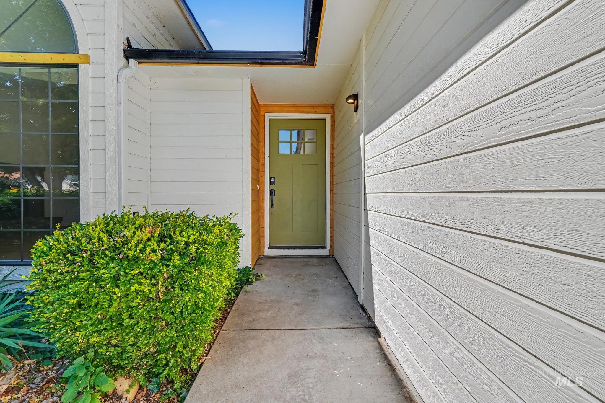 Front entry featuring a light green paneled door with glass inserts, side wall sconce, and concrete walkway
