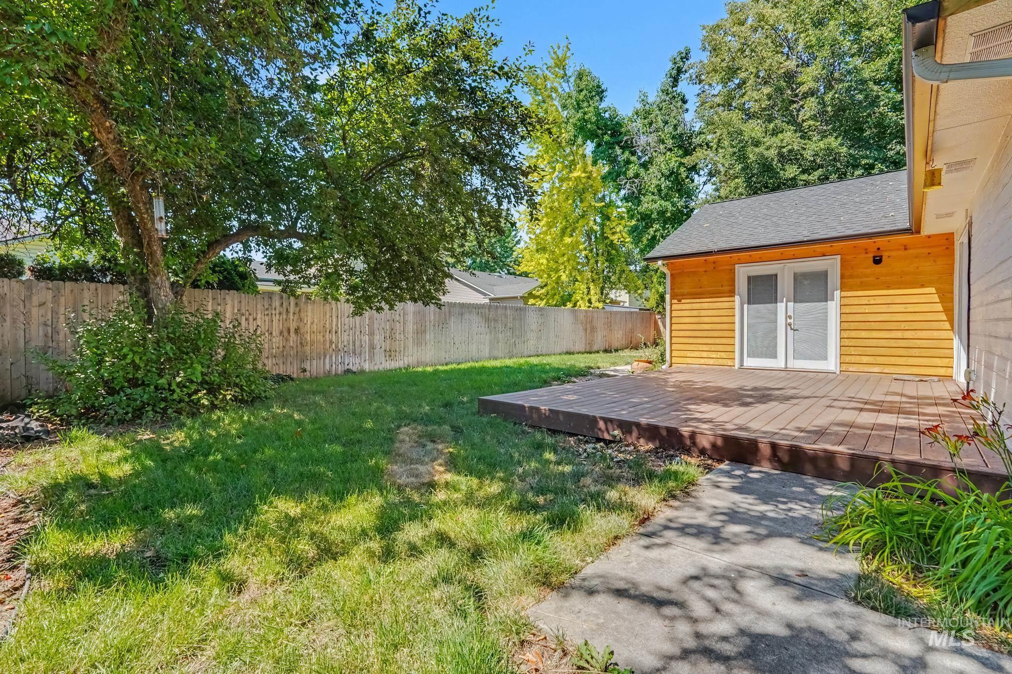 Expansive backyard featuring a wood-finish deck, verdant lawn, mature trees, and a privacy fence