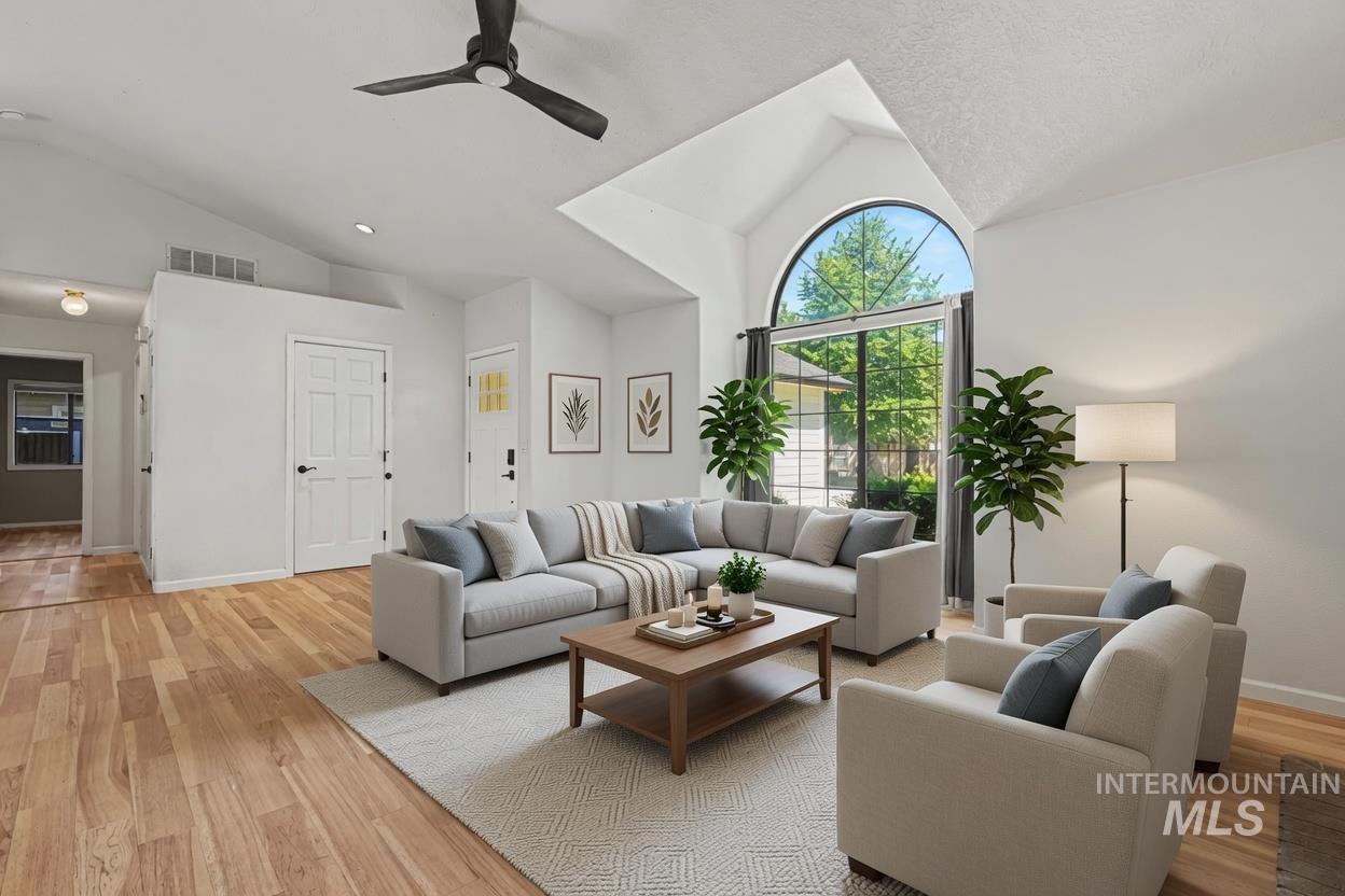 Living area featuring vaulted ceilings with a ceiling fan, a large arched window, and wood-finish flooring. *Virtually Staged photo*