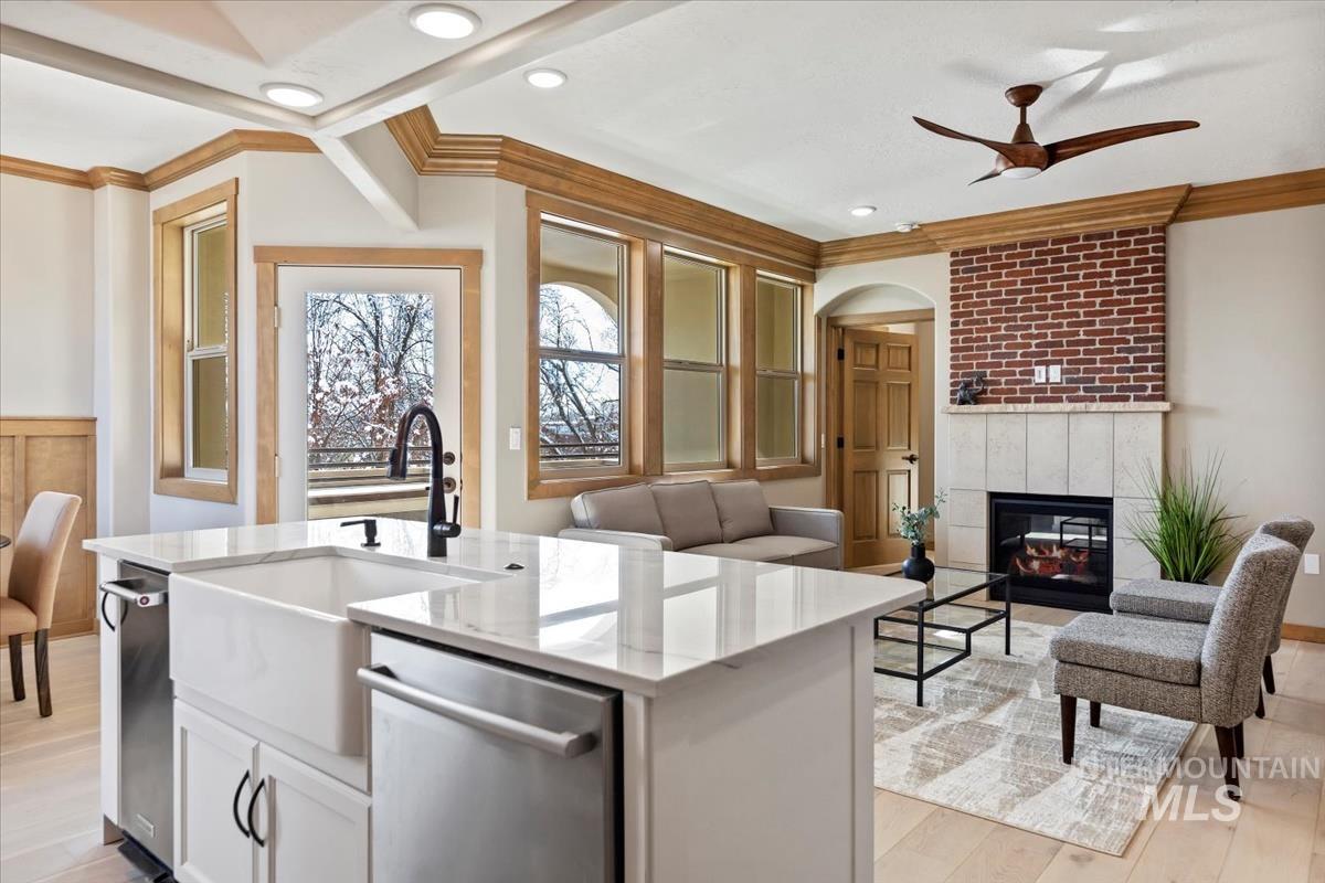 Kitchen with stainless steel dishwasher, open floor plan, crown molding, a ceiling fan, and light stone counters