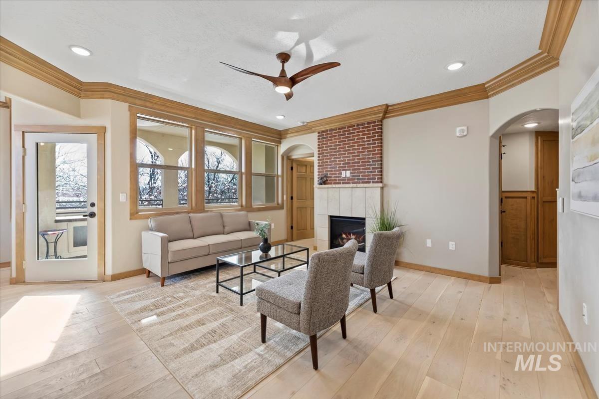 Living room featuring arched walkways, ceiling fan, crown molding, light wood-style floors, and a tiled fireplace