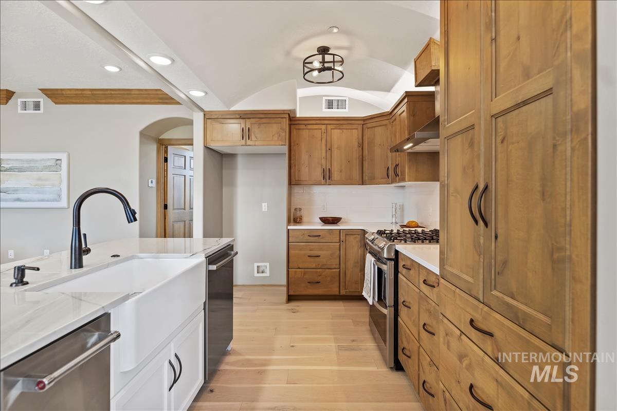 Kitchen featuring appliances with stainless steel finishes, light wood-style flooring, arched walkways, light stone counters, and vaulted ceiling