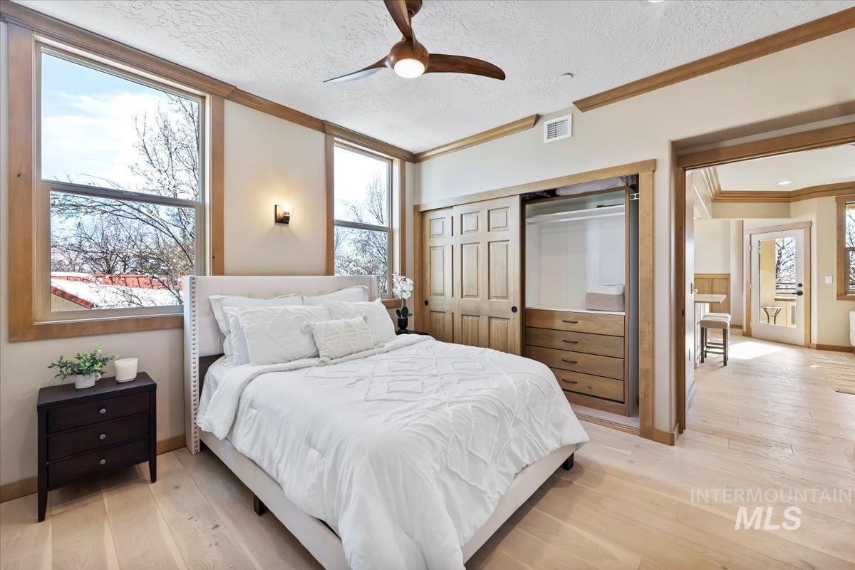 Bedroom featuring ornamental molding, light wood-style floors, a textured ceiling, a closet, and a ceiling fan