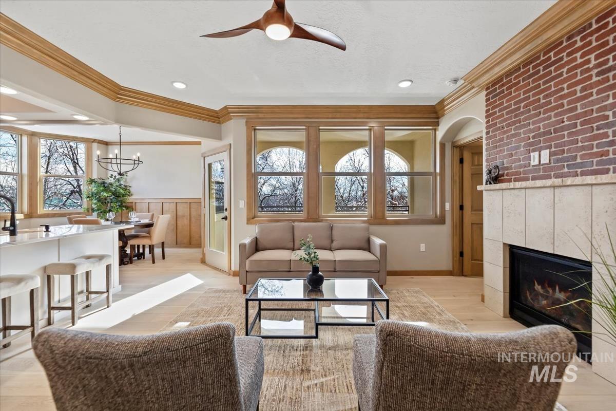 Living room featuring ornamental molding, a ceiling fan, wainscoting, a fireplace, and light wood finished floors