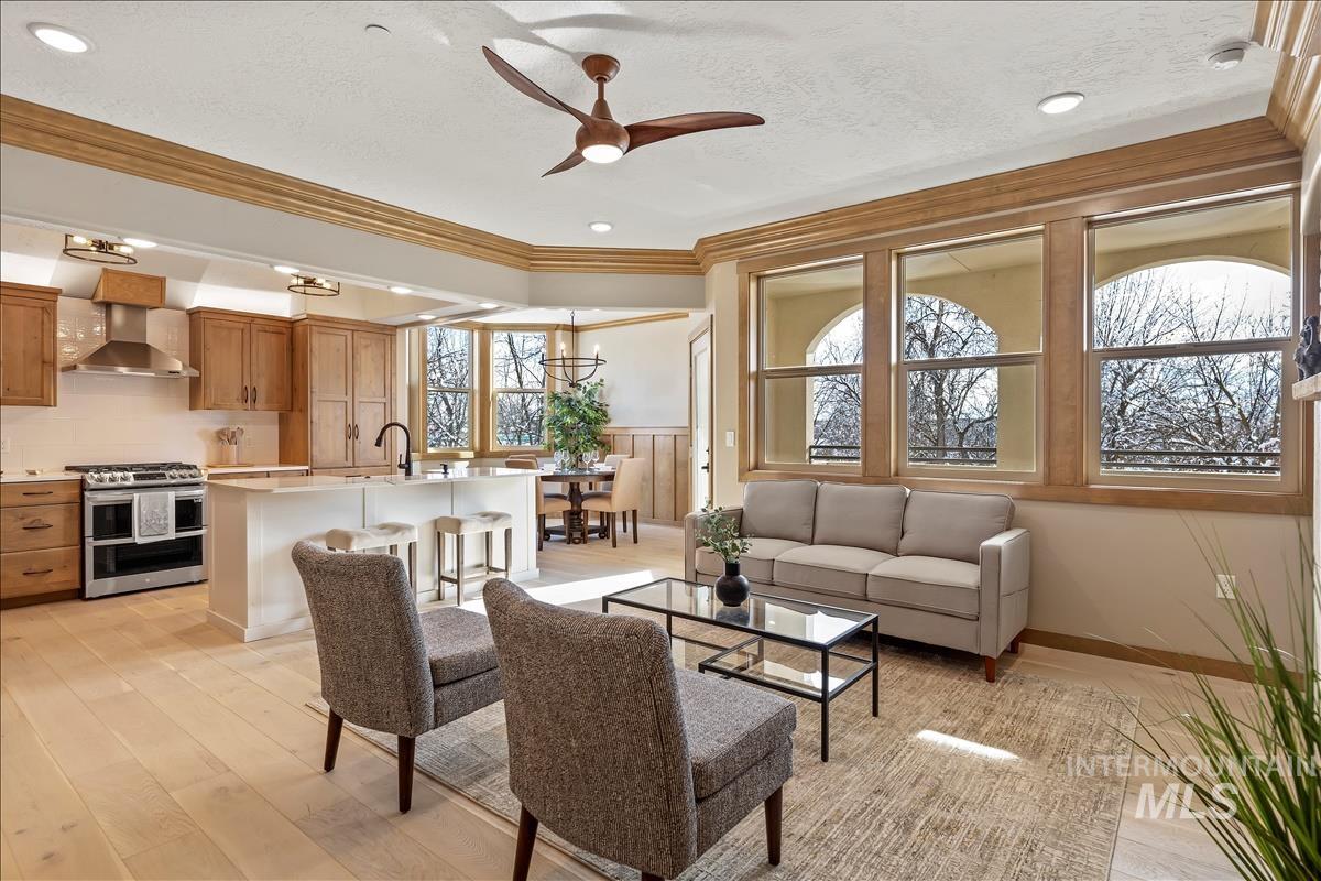 Living area featuring crown molding, a ceiling fan, a textured ceiling, light wood-style flooring, and wainscoting