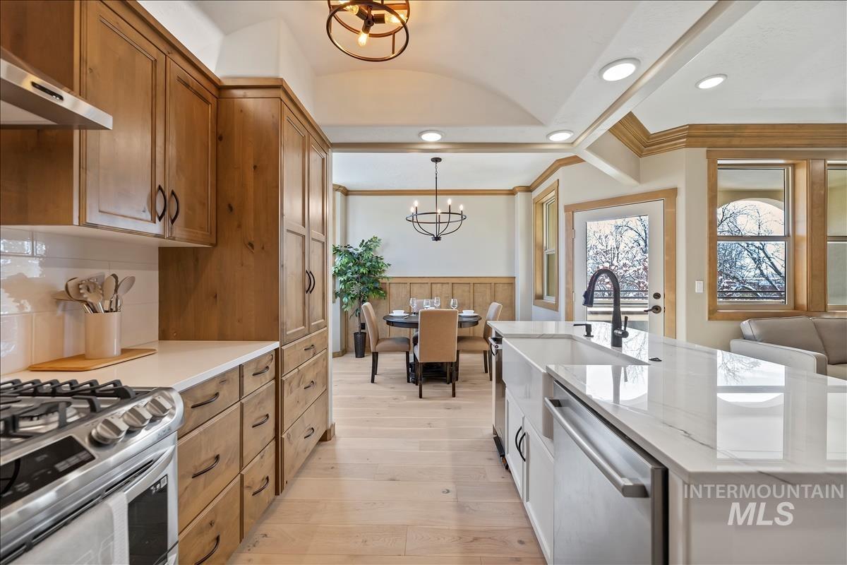 Kitchen featuring stainless steel appliances, range hood, a chandelier, wainscoting, and light wood-type flooring