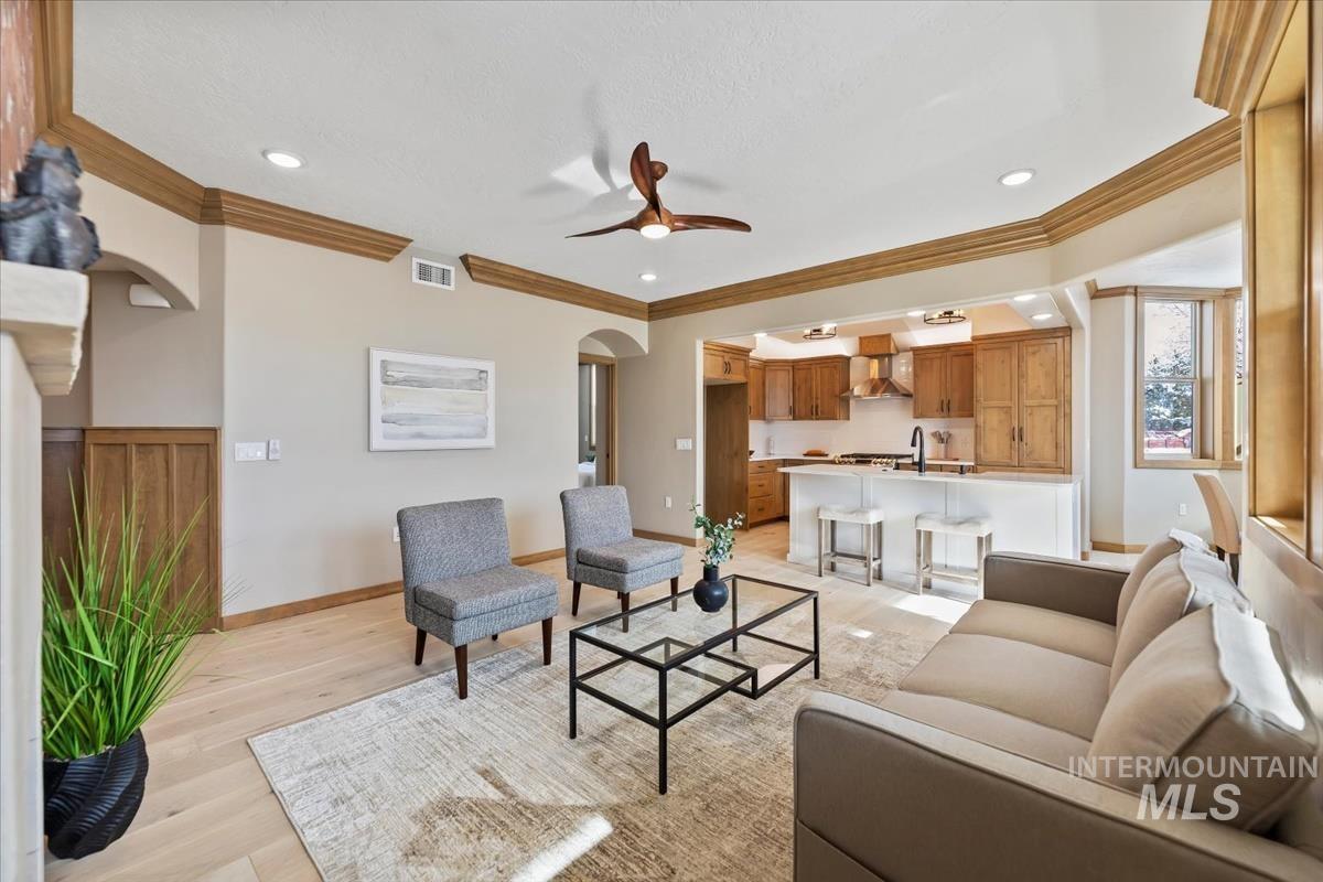Living room with arched walkways, light wood-style floors, ceiling fan, crown molding, and recessed lighting