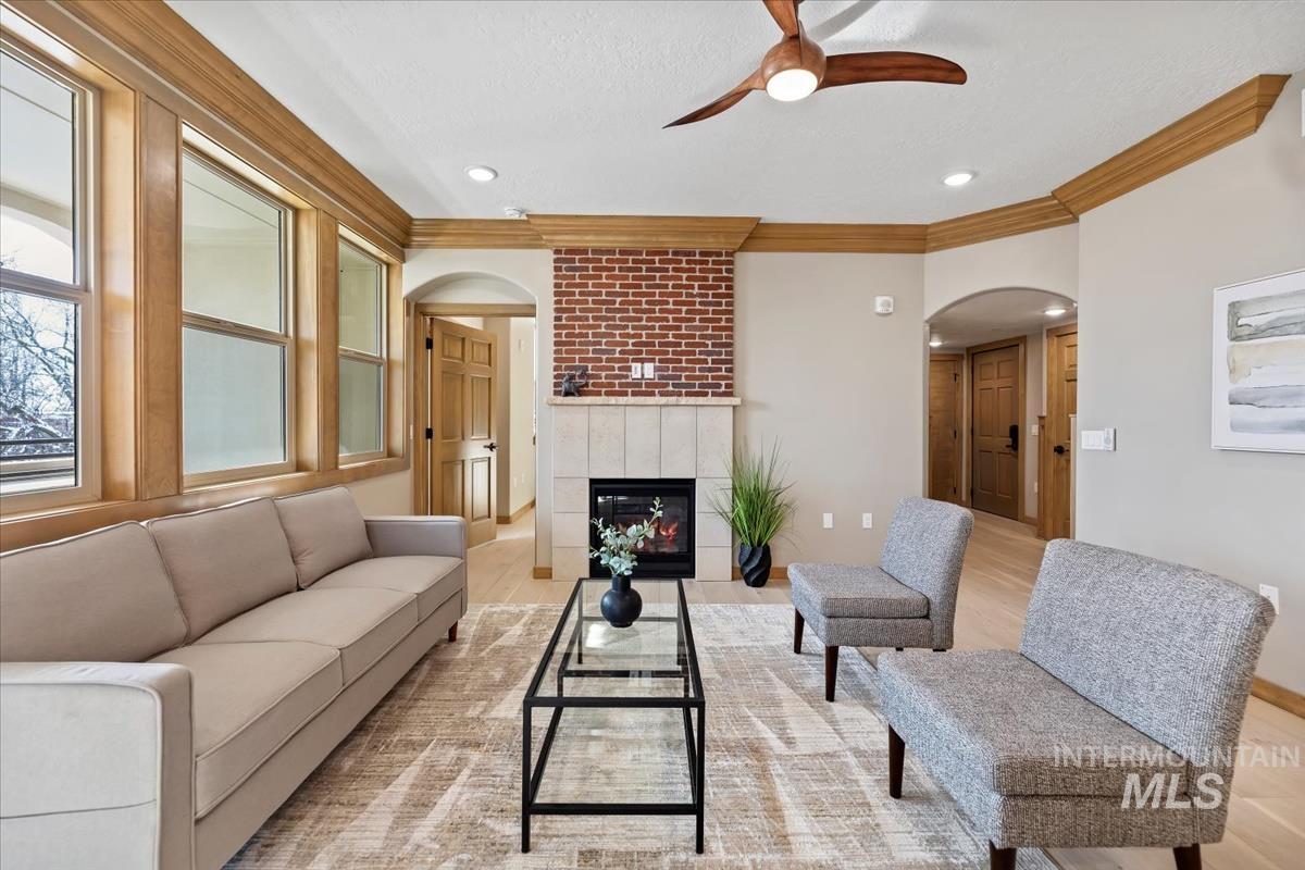Living area featuring arched walkways, crown molding, ceiling fan, light wood-type flooring, and a tile fireplace