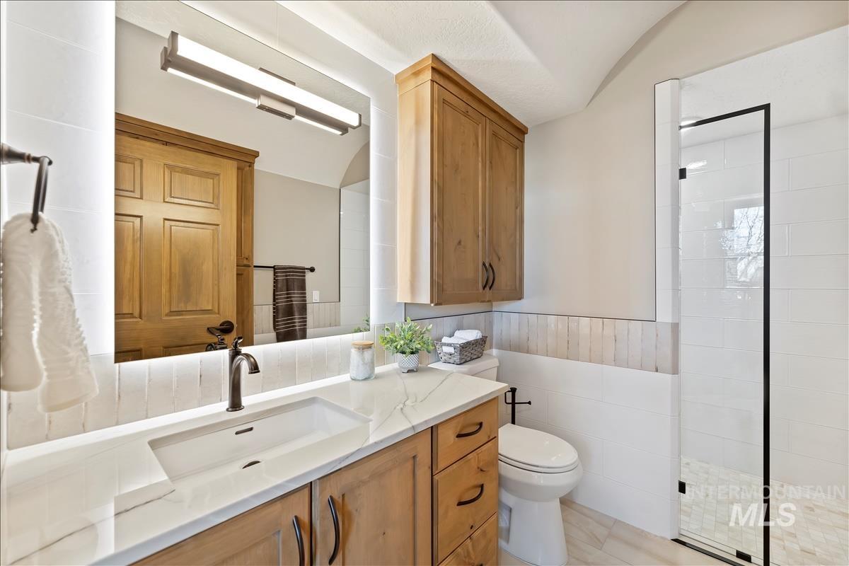 Bathroom featuring vanity, tiled shower, lofted ceiling, tile walls, and wainscoting
