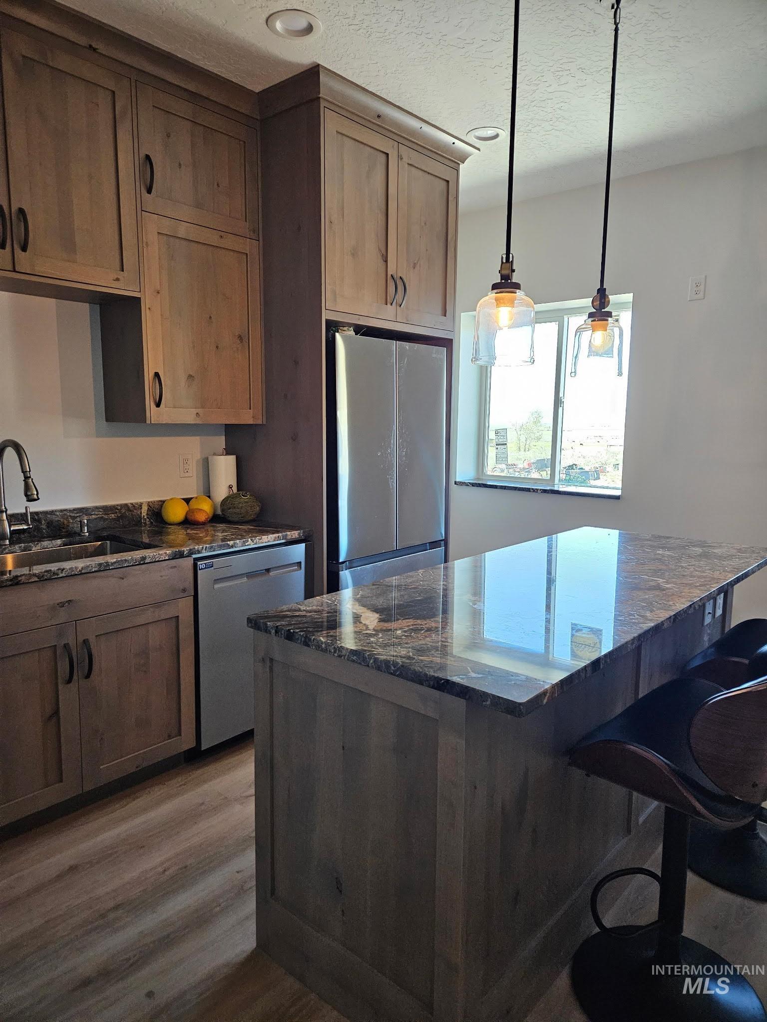 Kitchen with granite counters, a breakfast bar area, appliances with stainless steel finishes, a textured ceiling, and LVP floors