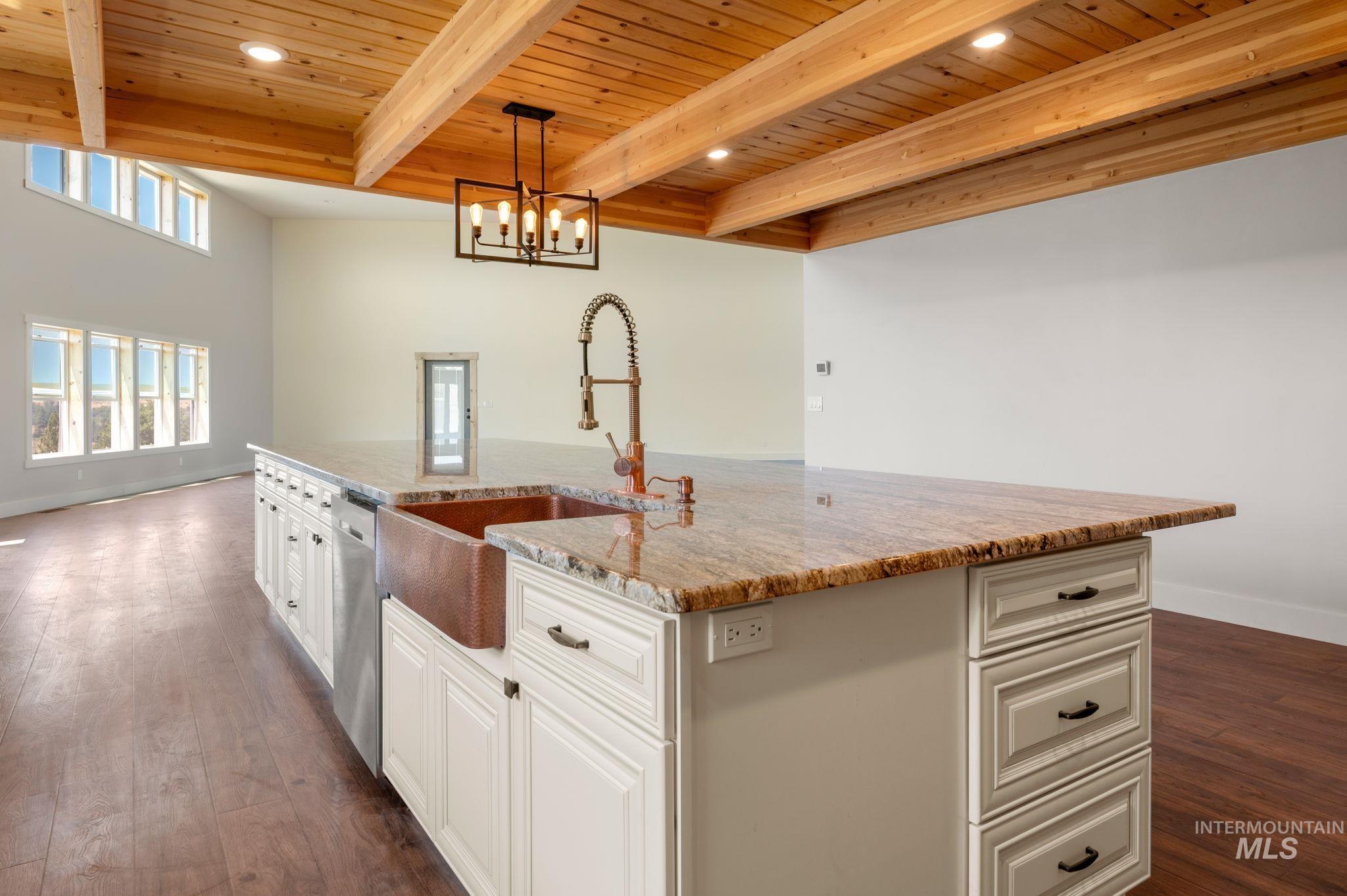 Kitchen featuring a large island, a wooden ceiling with exposed beams, hanging light fixtures, light stone countertops, and white cabinetry