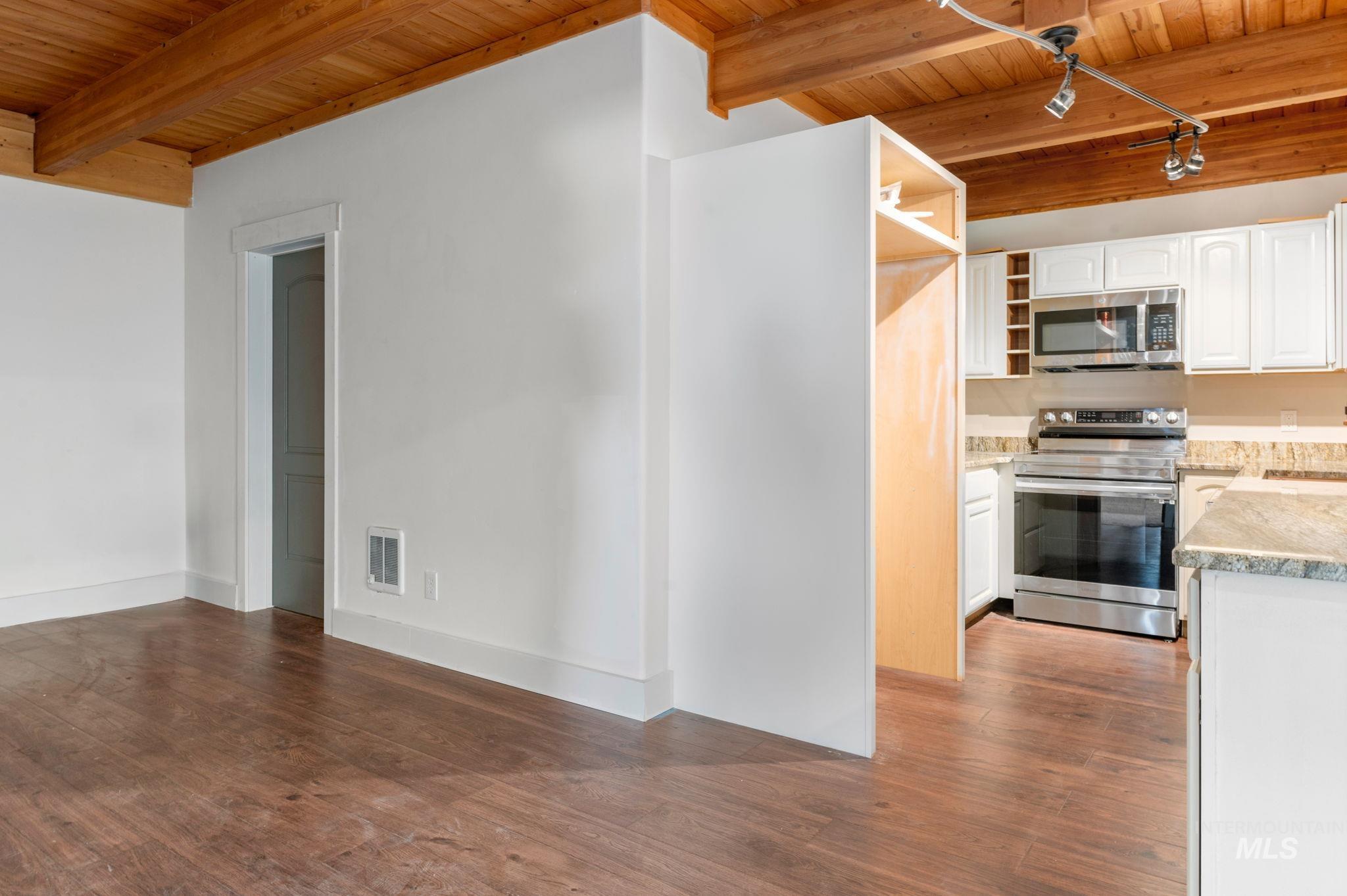 Kitchen with a wooden ceiling with exposed beams, open shelves, stainless steel appliances, white cabinets, and light stone counters