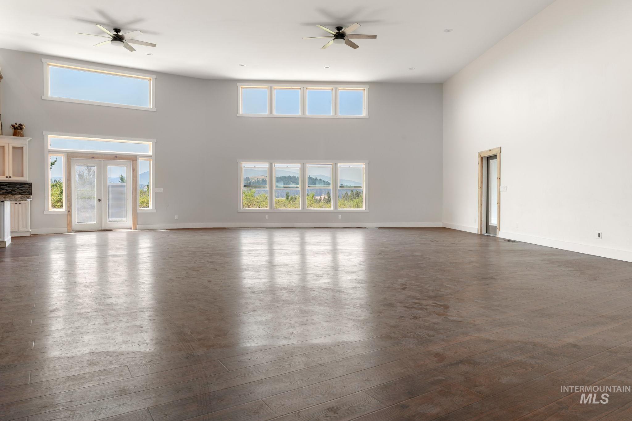 Unfurnished living room featuring ceiling fan, a high ceiling, dark wood-type flooring, and french doors