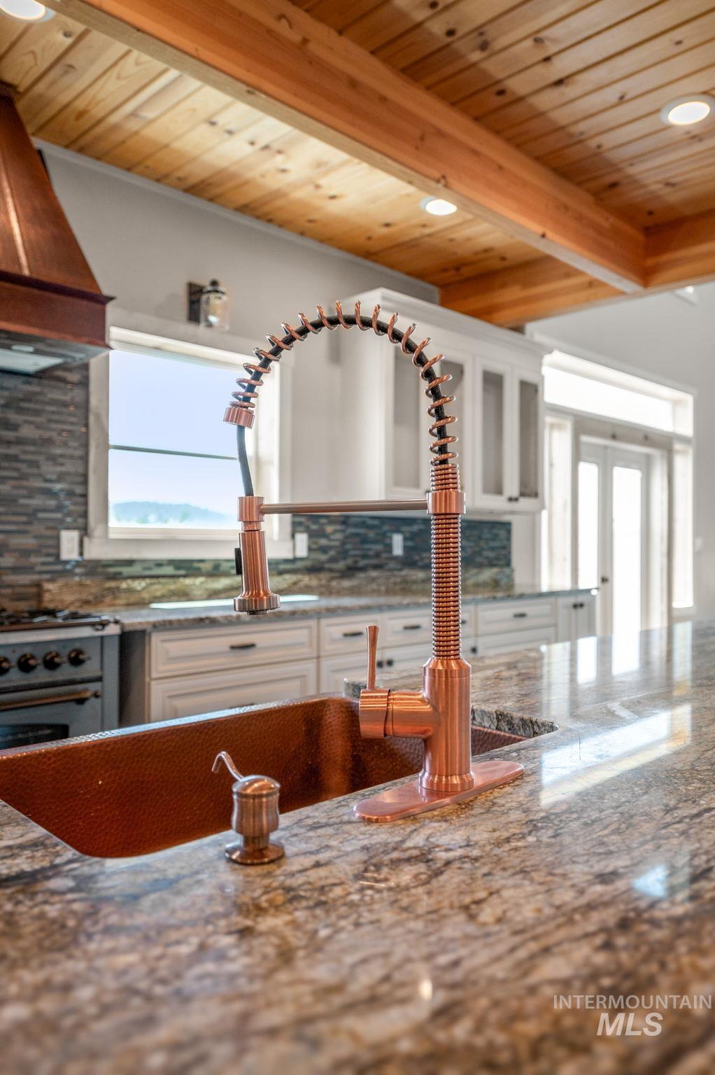 Kitchen with dark stone counters, decorative backsplash, a wood ceiling with exposed beams, stainless steel gas range oven, and premium range hood