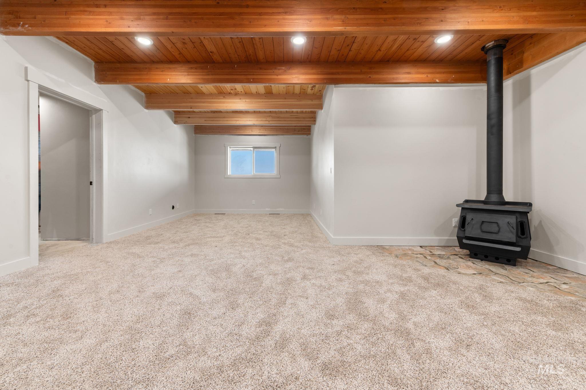 Basement featuring a wood stove, light colored carpet, wooden ceiling, and recessed lighting