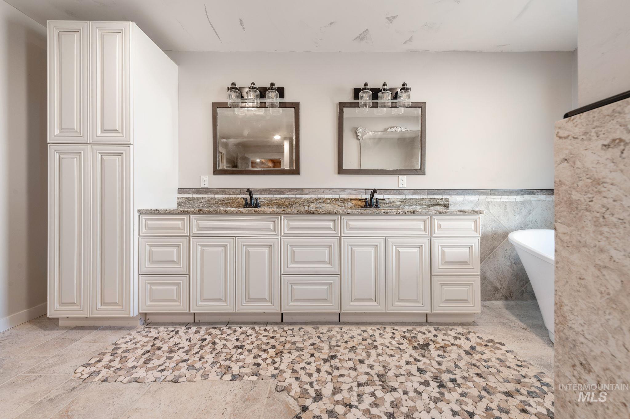 Full bathroom featuring tile walls, double vanity, a freestanding bath, and wainscoting