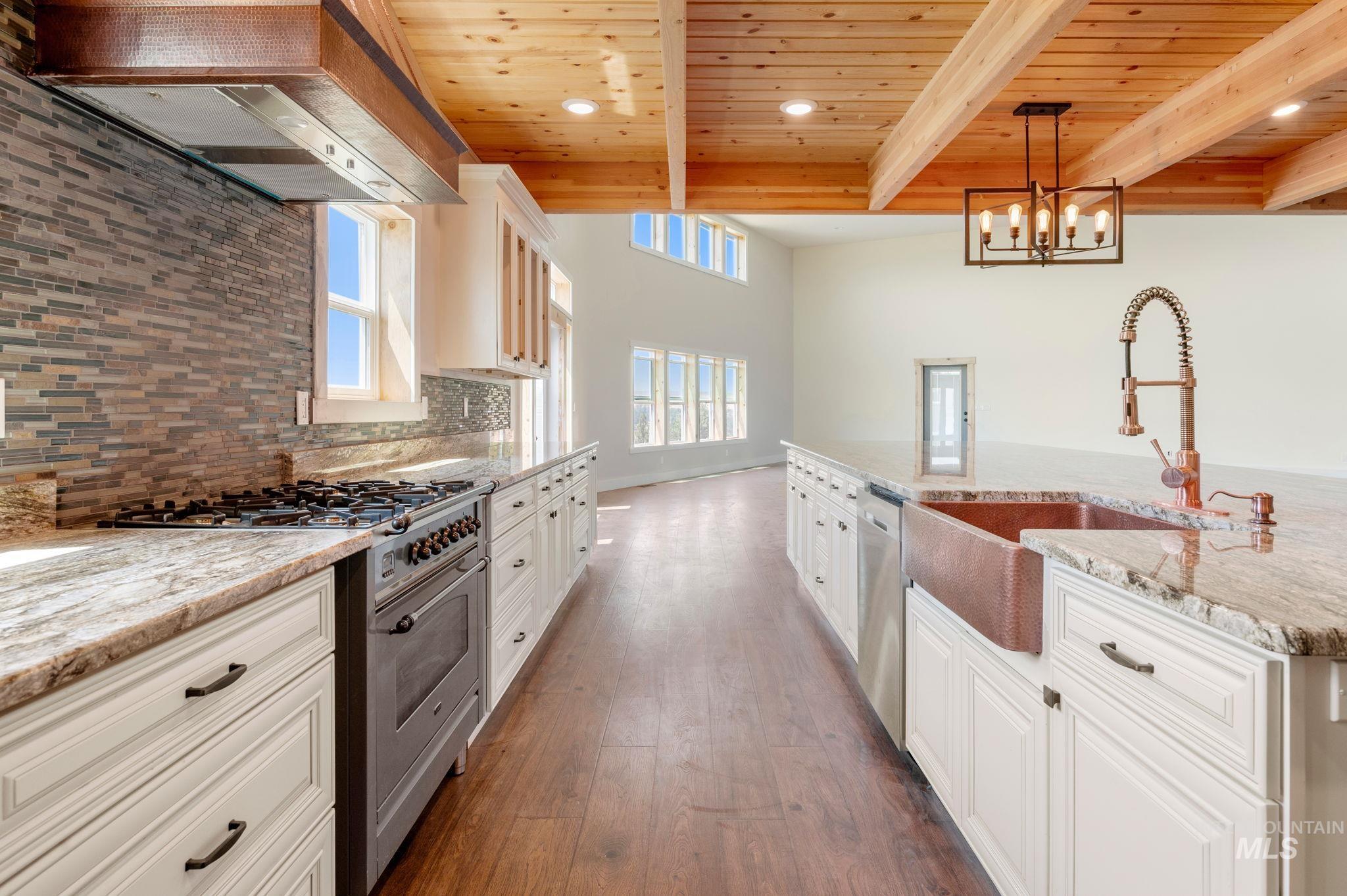 Kitchen with stainless steel appliances, light stone counters, custom range hood, a spacious island, and white cabinetry