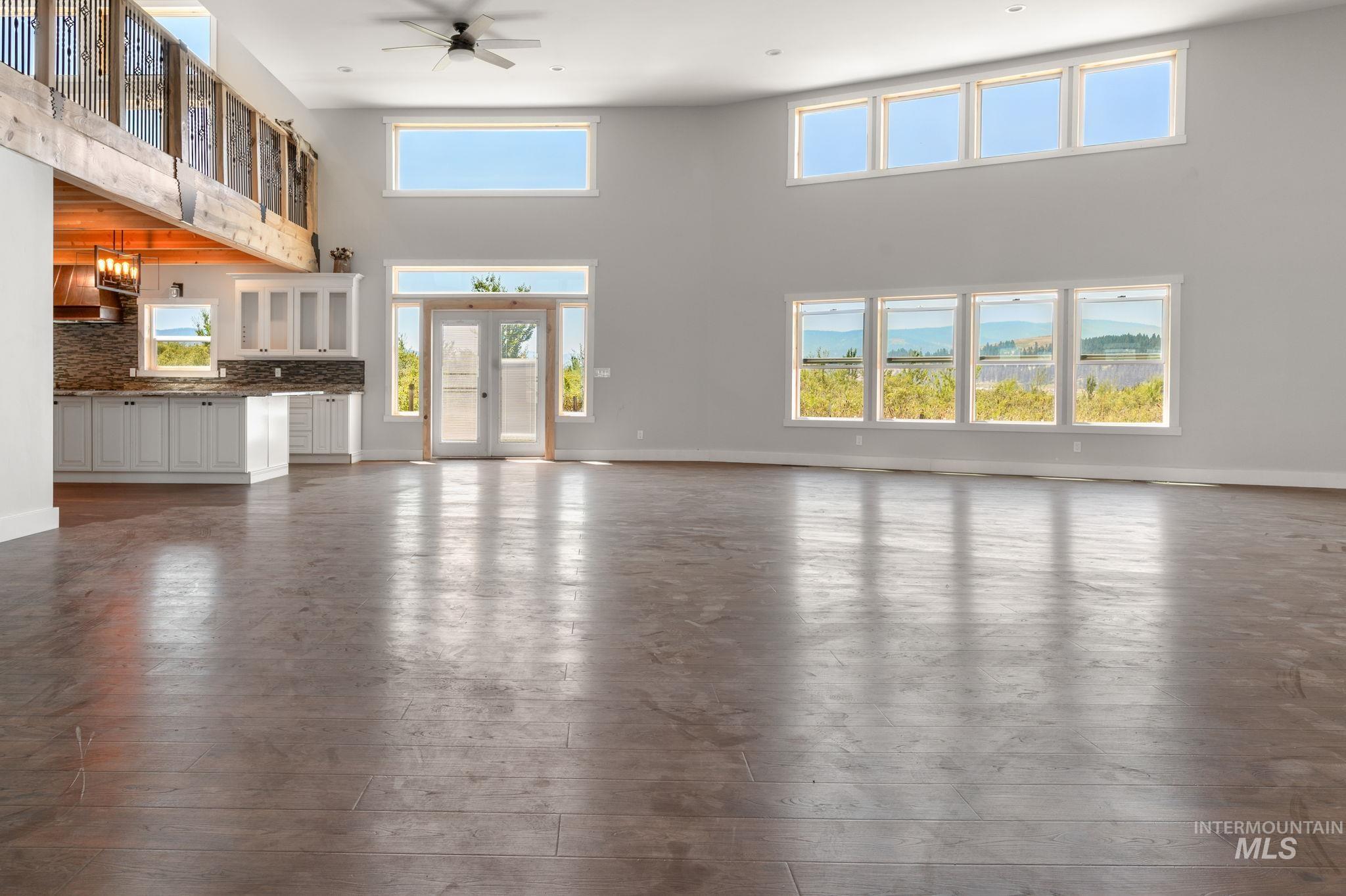 Unfurnished living room featuring a towering ceiling, dark wood-type flooring, a ceiling fan, and french doors
