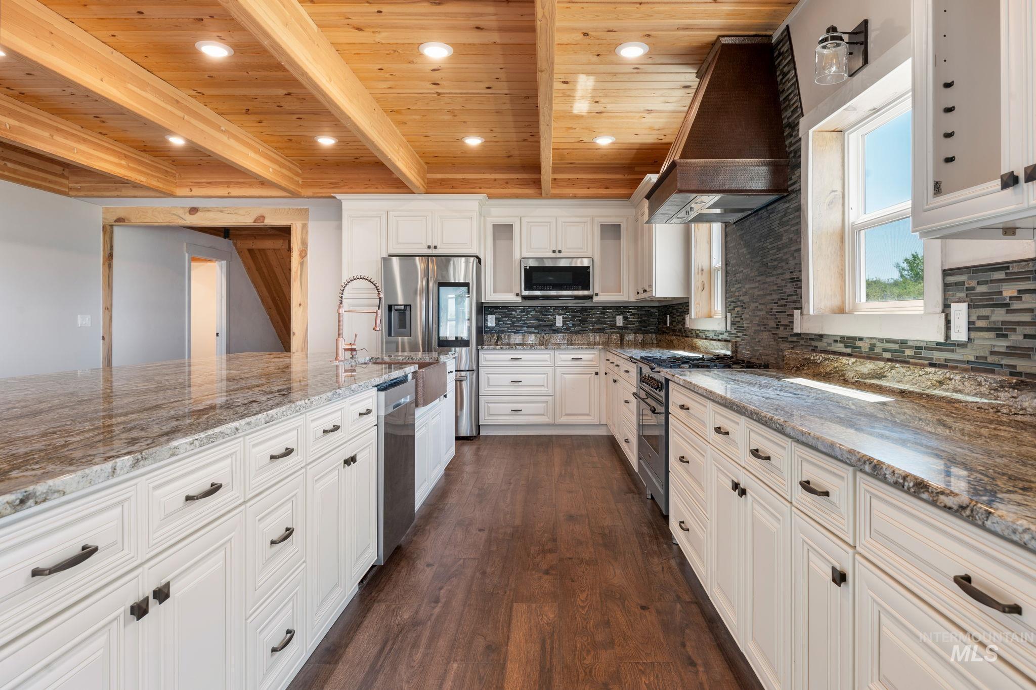 Kitchen with custom exhaust hood, dark wood-style floors, white cabinets, light stone countertops, and decorative backsplash