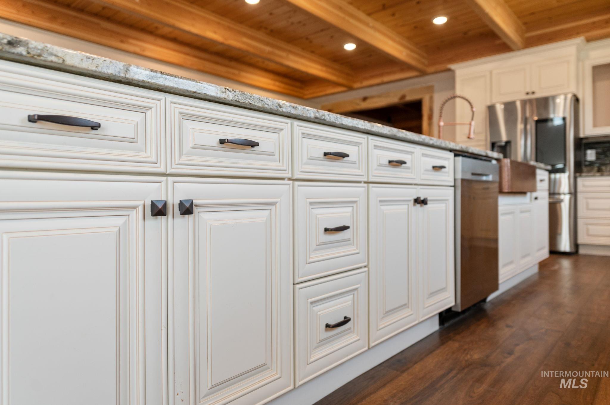 Kitchen view of a wooden ceiling with exposed beams, stainless steel appliances, white cabinets, dark wood-style flooring, and recessed lighting