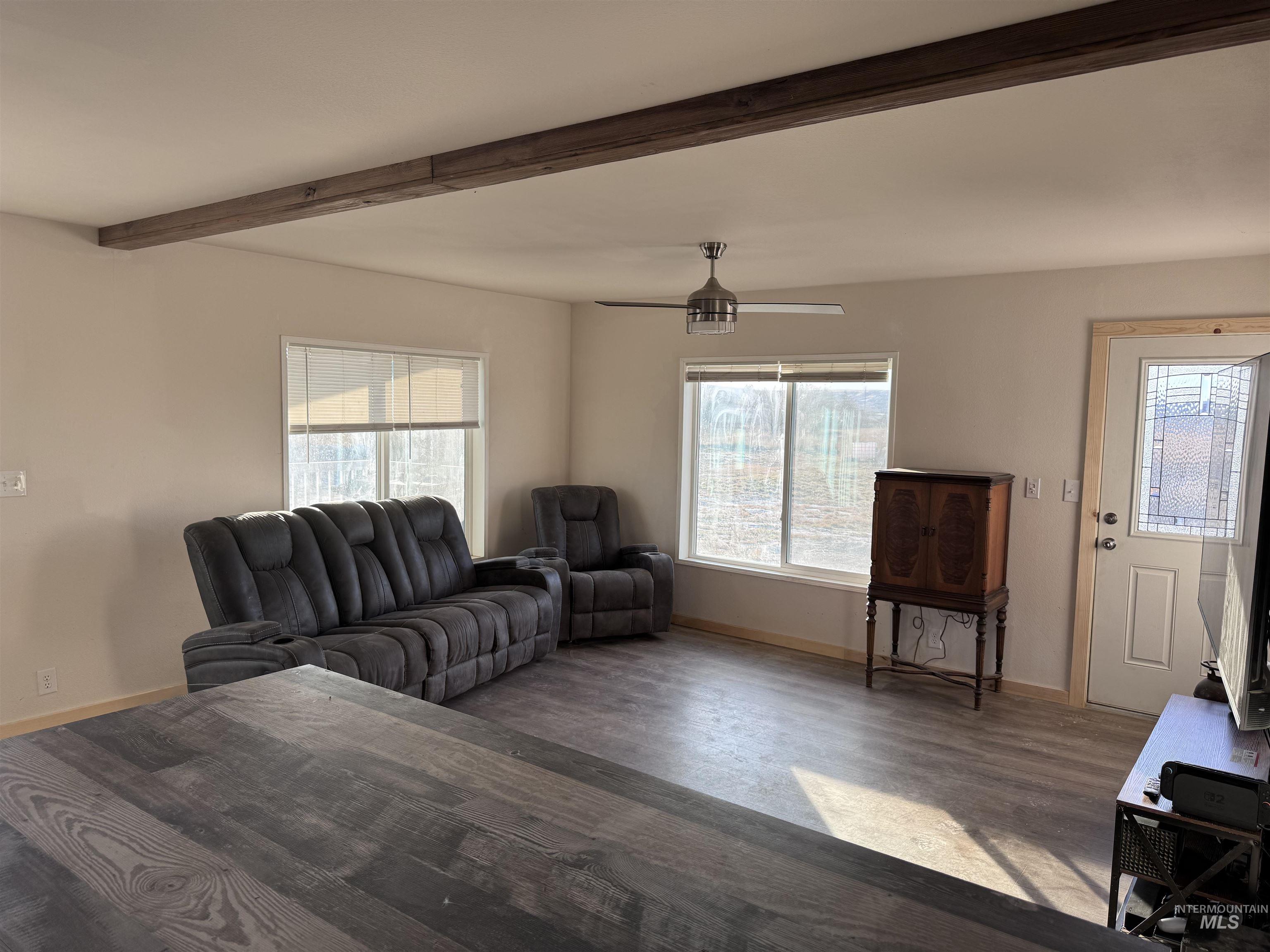Living area with wood finished floors, a ceiling fan, and beamed ceiling