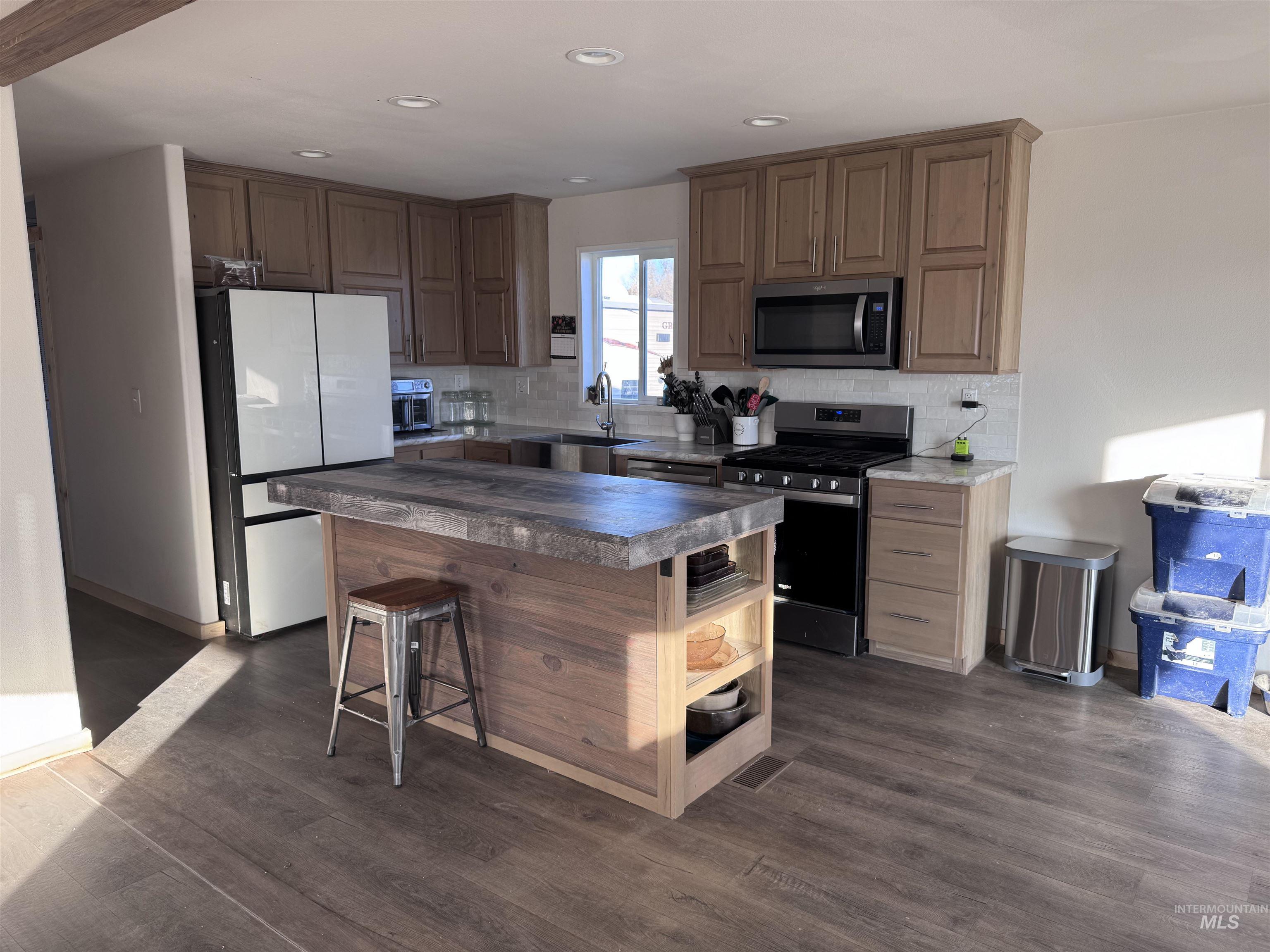 Kitchen featuring decorative backsplash, electric range, freestanding refrigerator, dark wood-type flooring, and stainless steel microwave