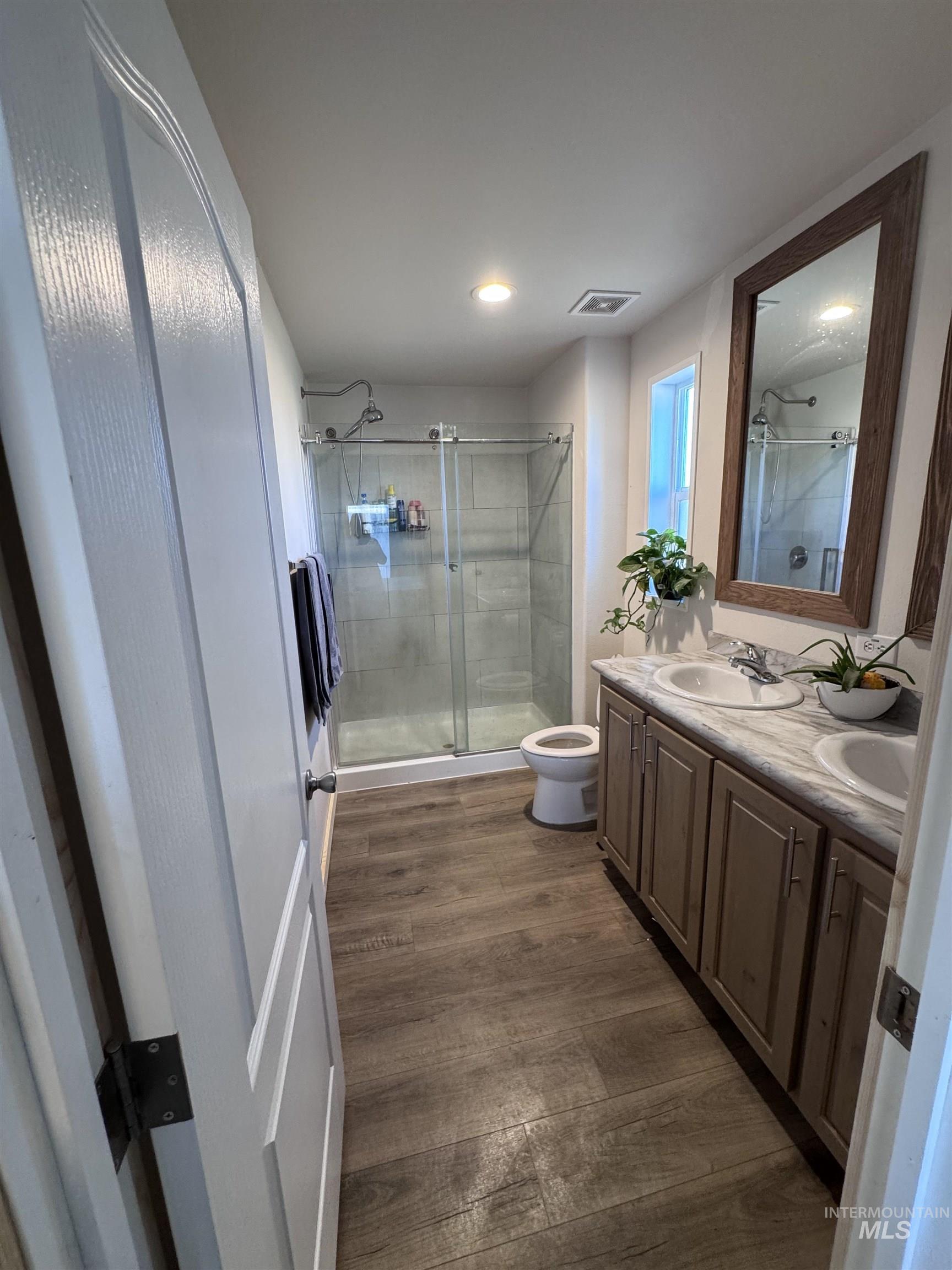 Bathroom featuring dark wood finished floors, double vanity, and a shower stall