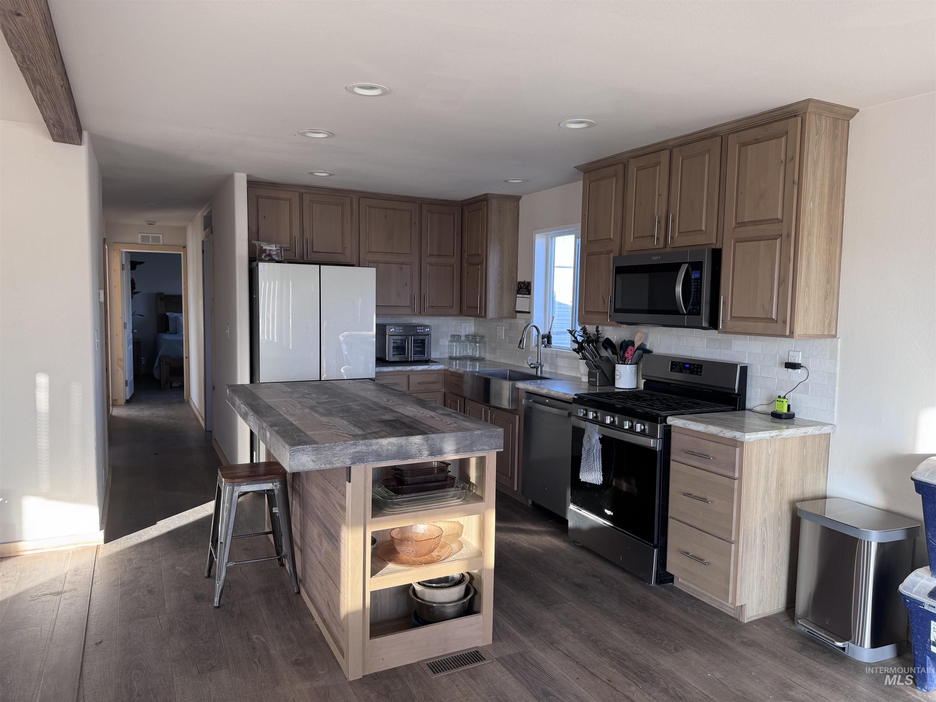 Kitchen with appliances with stainless steel finishes, a breakfast bar area, dark wood-type flooring, tasteful backsplash, and a kitchen island