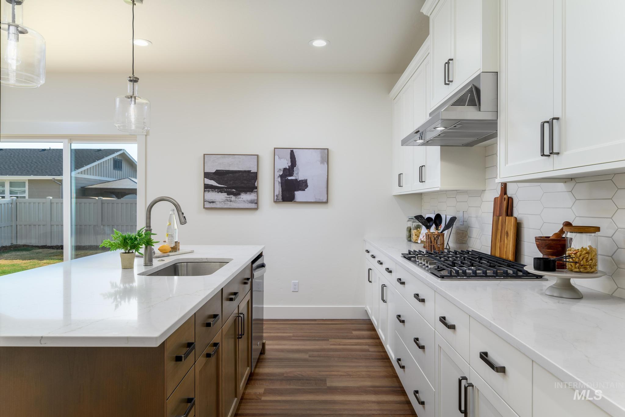 Kitchen featuring white cabinetry, hanging light fixtures, an island with sink, dark wood-style flooring, and light stone countertops