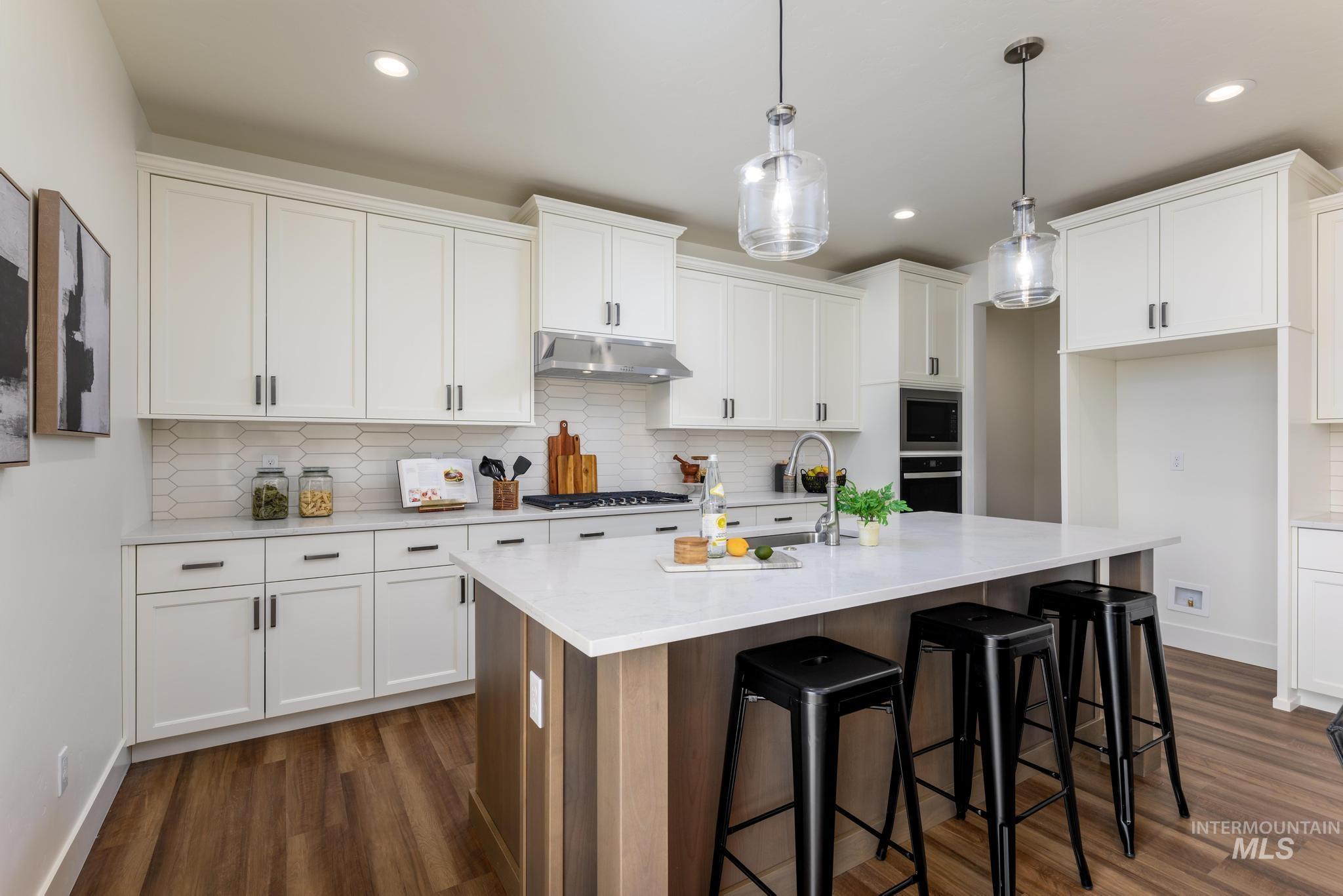 Kitchen with decorative backsplash, a center island with sink, dark wood finished floors, a kitchen bar, and under cabinet range hood