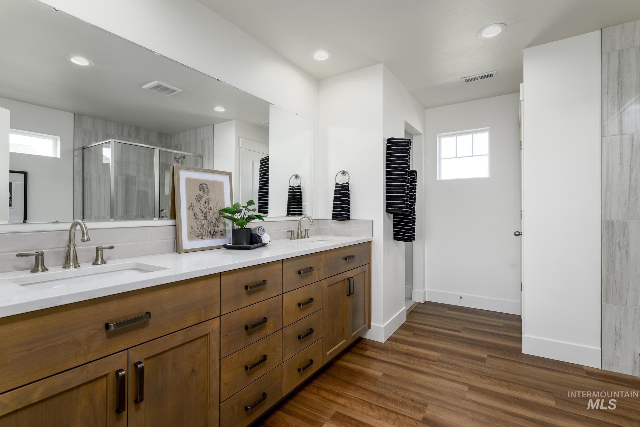 Full bath with plenty of natural light, a stall shower, dark wood finished floors, double vanity, and recessed lighting