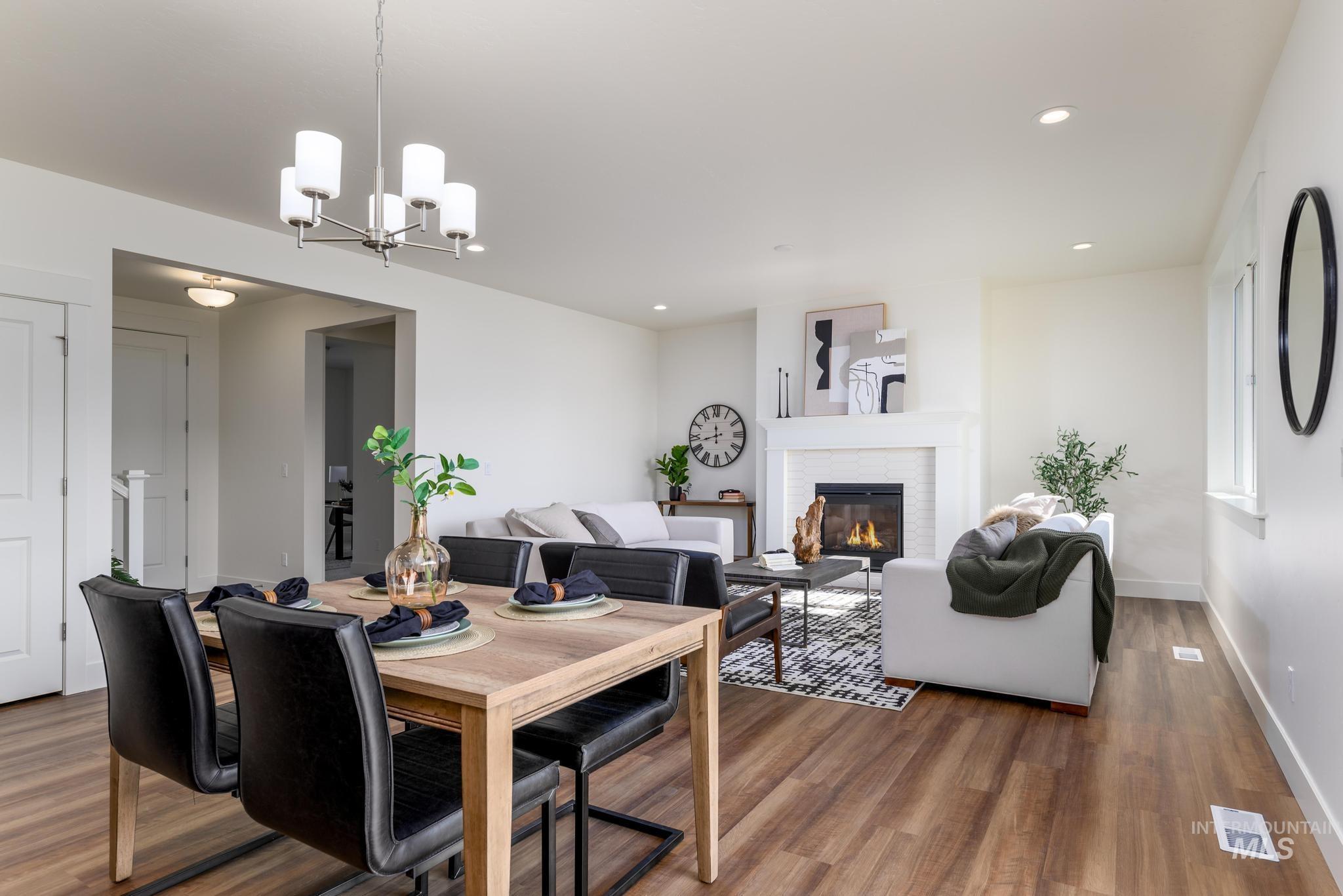 Dining space with wood finished floors, a stone fireplace, a chandelier, and recessed lighting