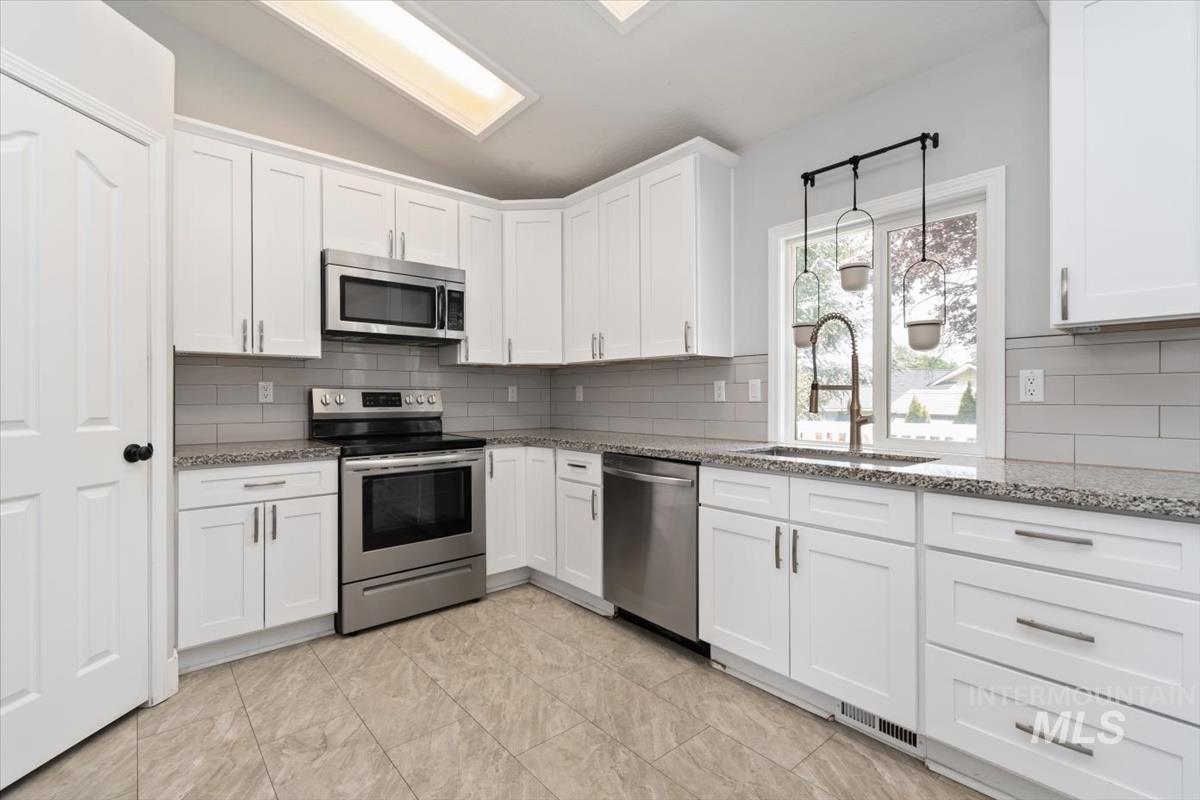 Kitchen featuring white cabinetry, stone-finish countertops, stainless steel appliances, grey subway tile backsplash, and tile flooring