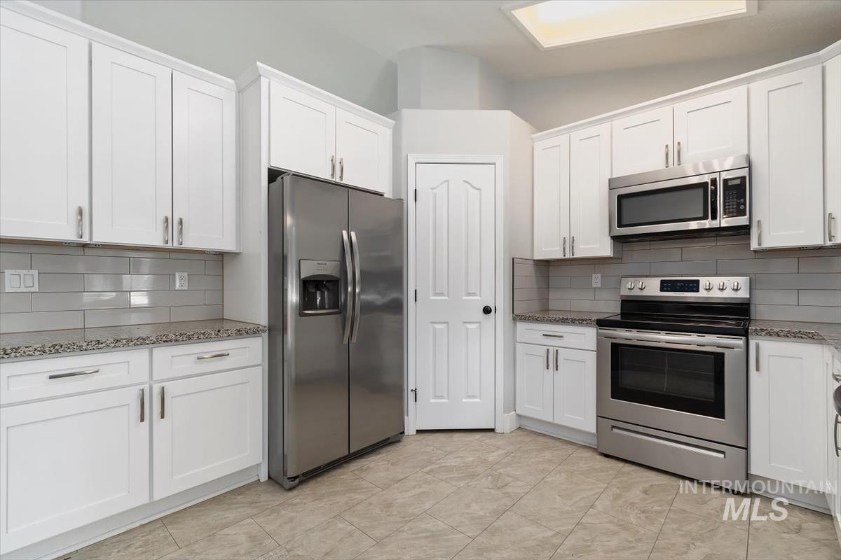 Bright kitchen featuring white shaker cabinetry, stainless steel appliances, speckled countertops, and a subway tile backsplash