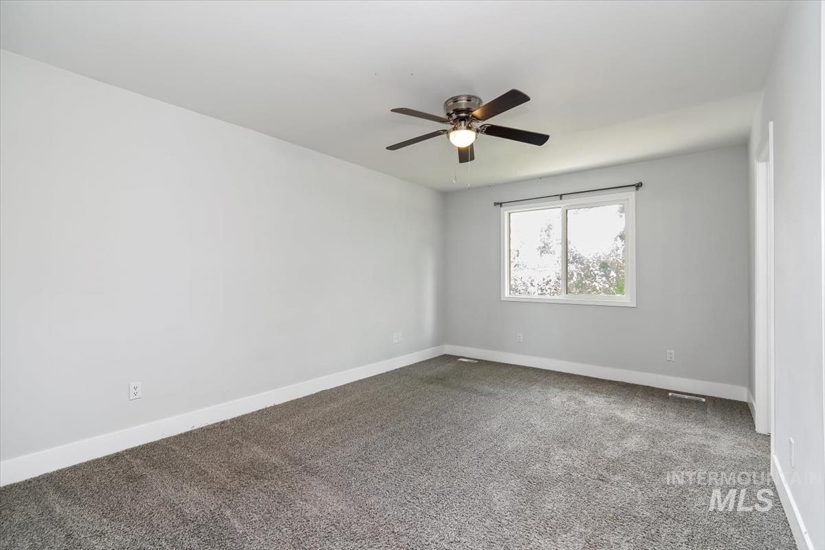 Spacious room featuring neutral gray carpeting, white baseboards, and light gray walls